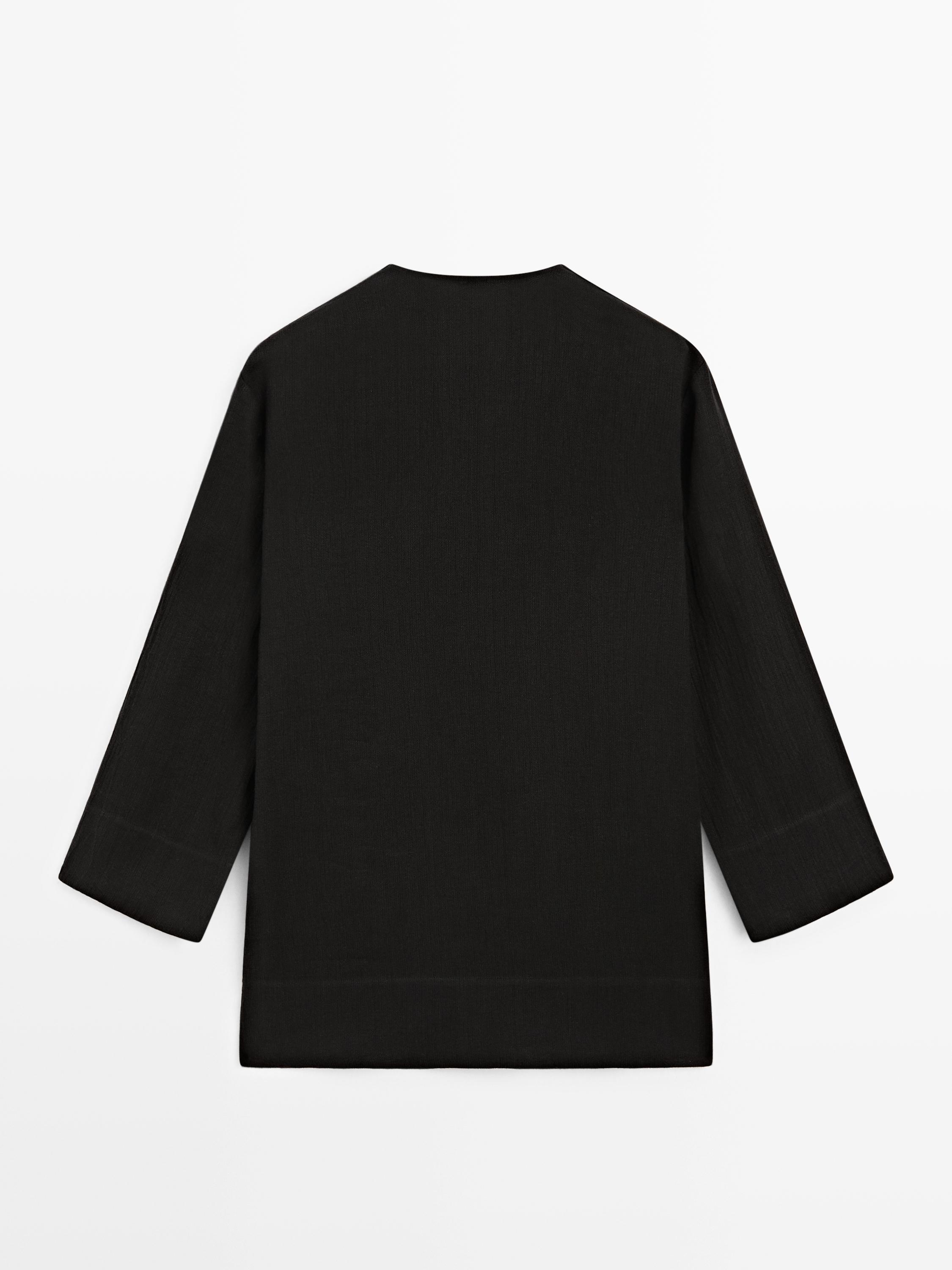 Vista posterior de una prenda negra de manga larga con corte recto y cuello redondo.