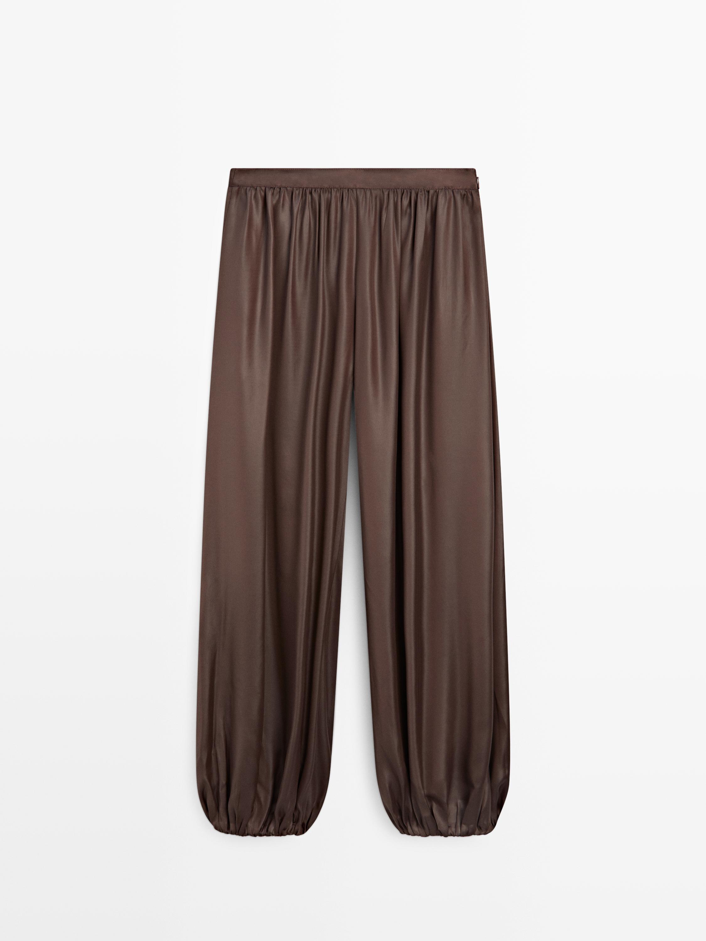 Vooraanzicht van een bruine satijnen broek met elastische tailleband en wijde pijpen die bij de enkels aansluiten.