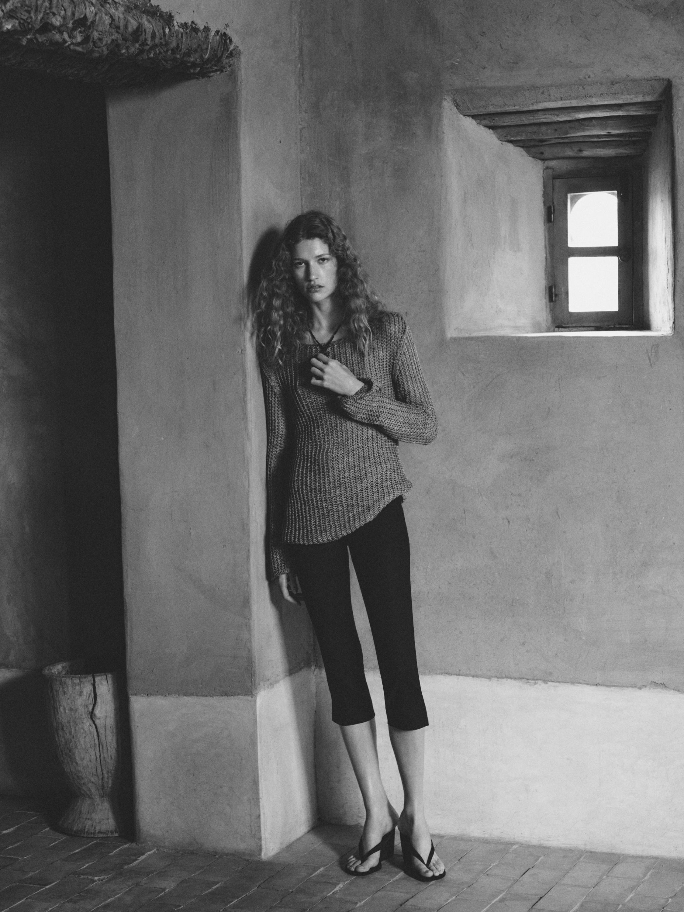 Conxunto de pantalón capri negro e xersei de punto gris, sandalias negras.