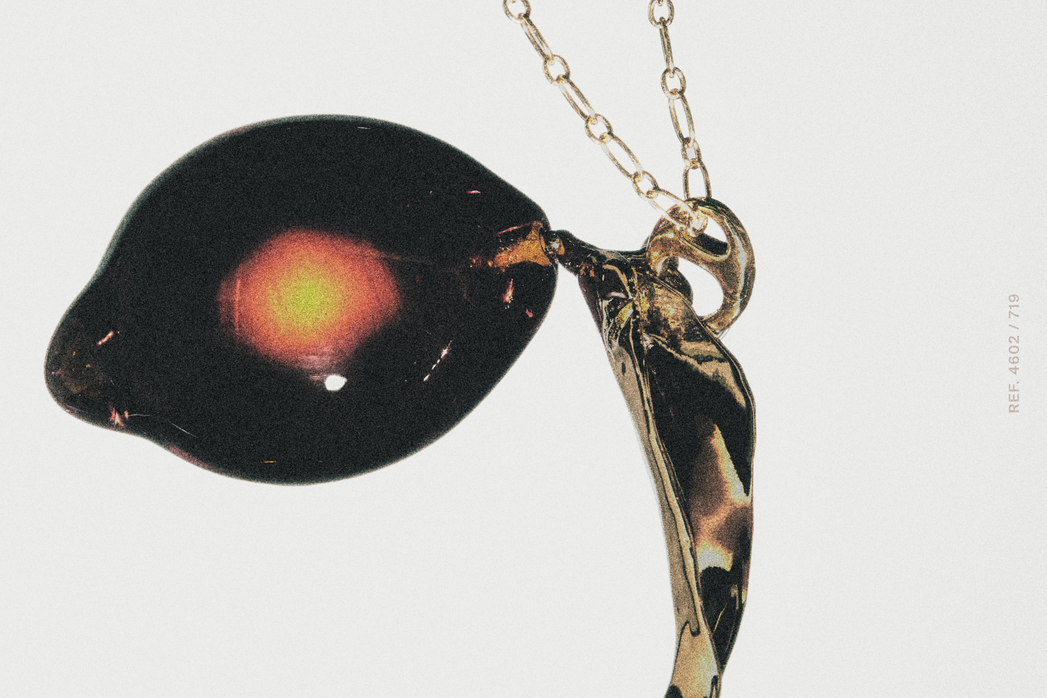 Detail van gouden ketting met donkerglazen hanger en fijne ketting.