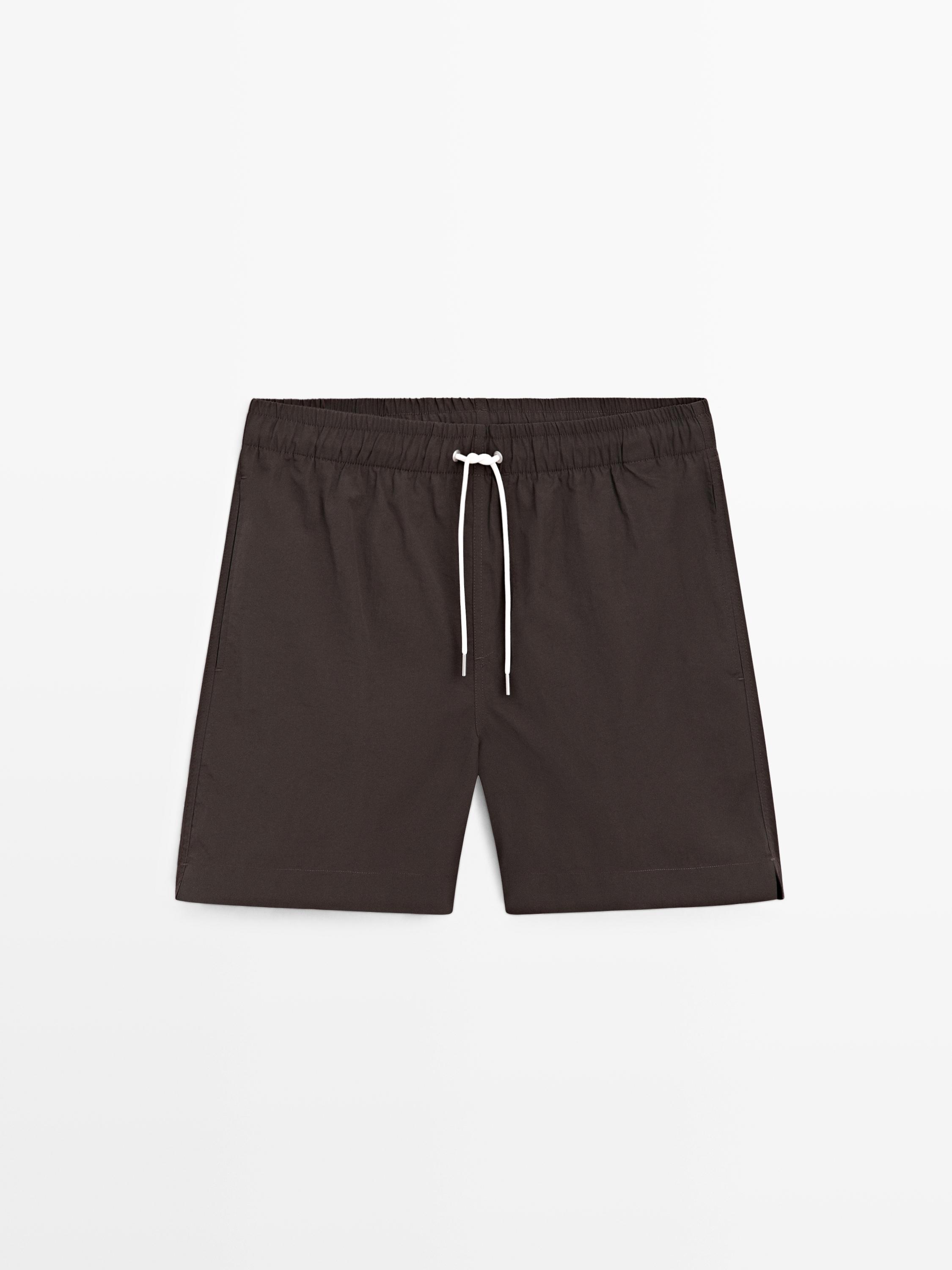 Vorderansicht einer braunen Badeshorts mit elastischem Bund und weißem Kordelzug. Sichtbare Seitentaschen.