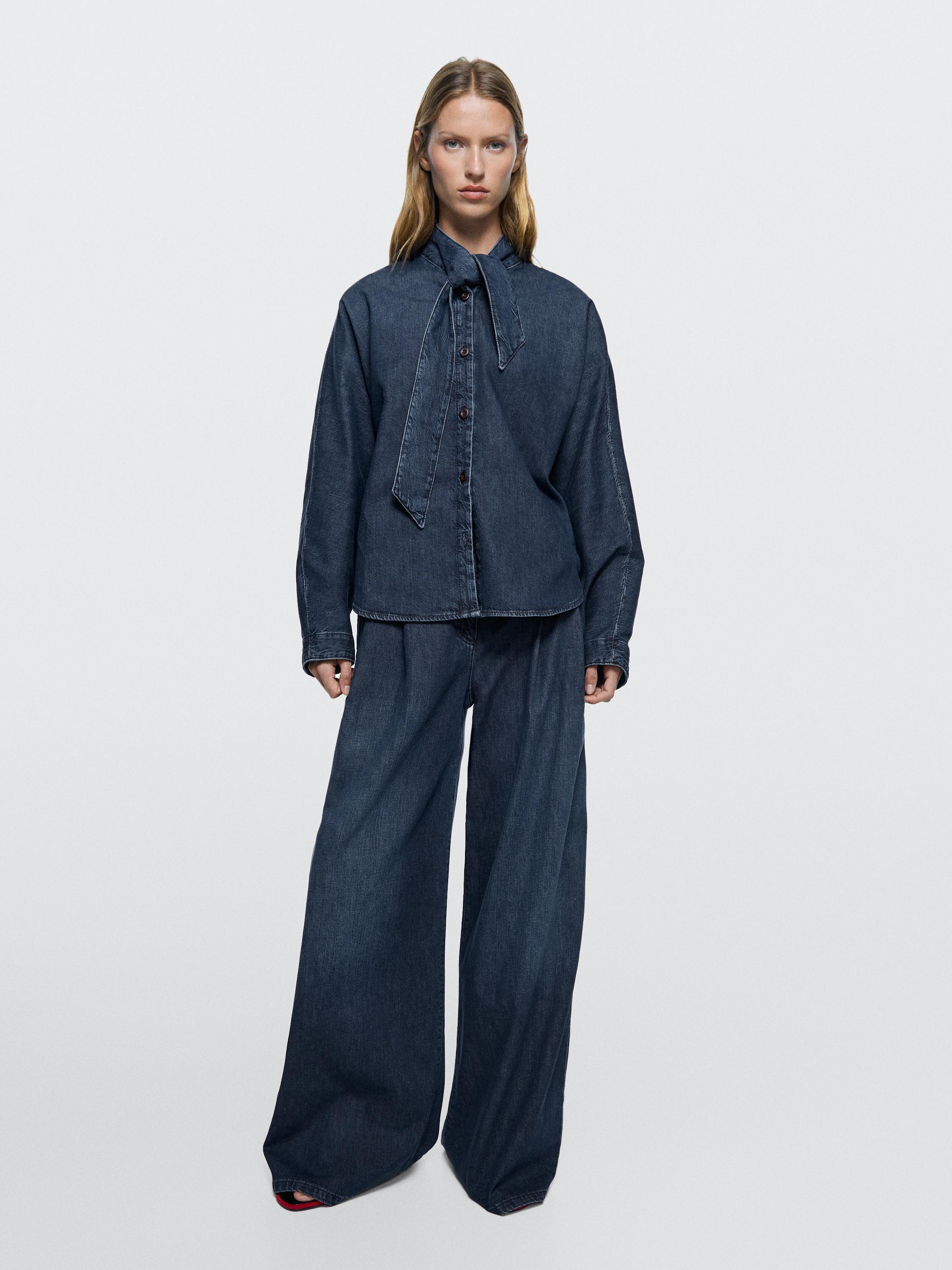 Donkerblauw shirt met strik en high-waist wide-leg jeans.