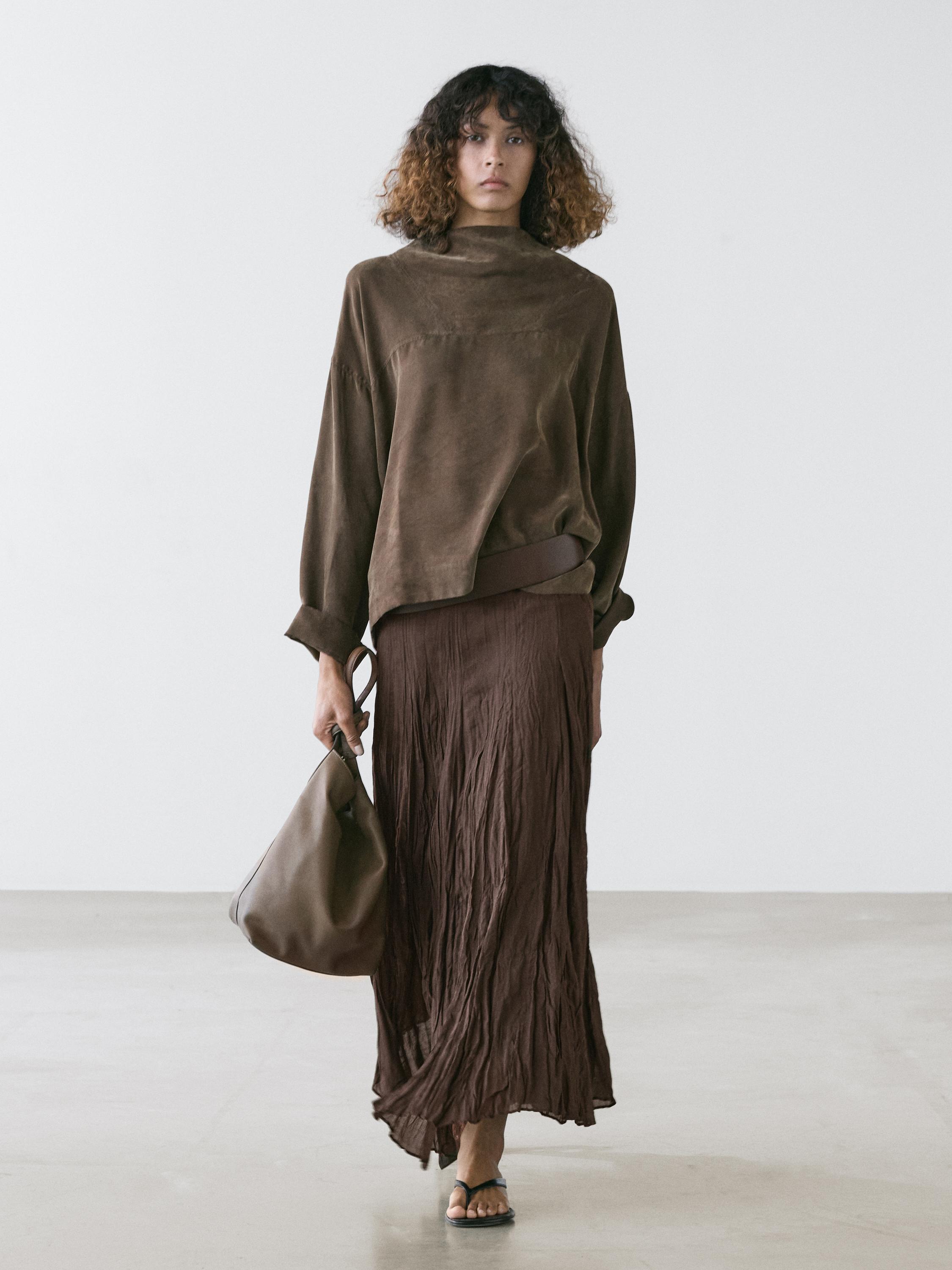 Set me këmishë ngjyrë kafe me jakë të lartë dhe mëngë të gjata, fund të gjatë me pala ngjyrë kafe dhe çantë ngjyrë kafe.