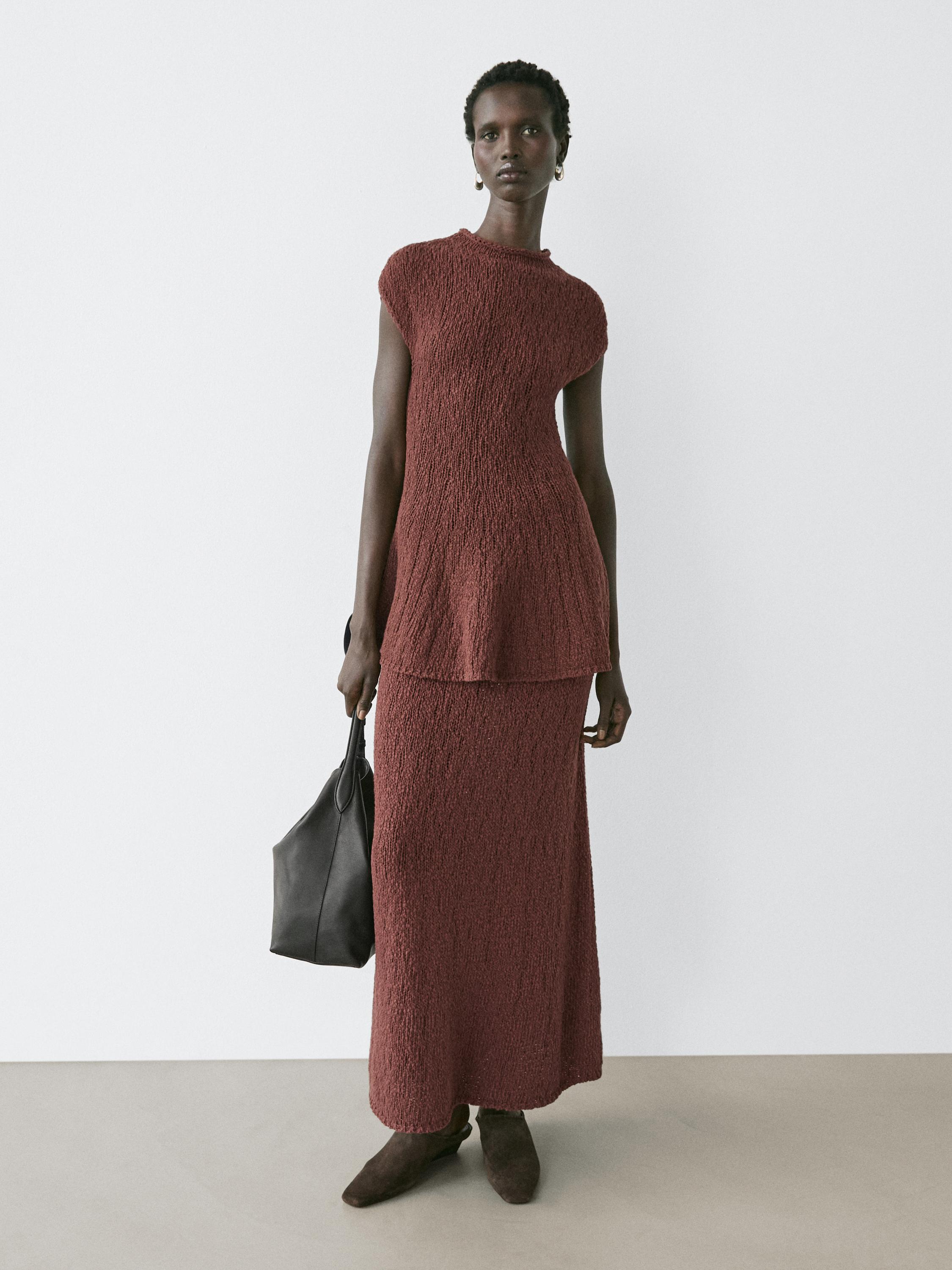 Conjunto de vestido largo marrón texturizado sin mangas y falda larga, con bolso negro y botines marrones.