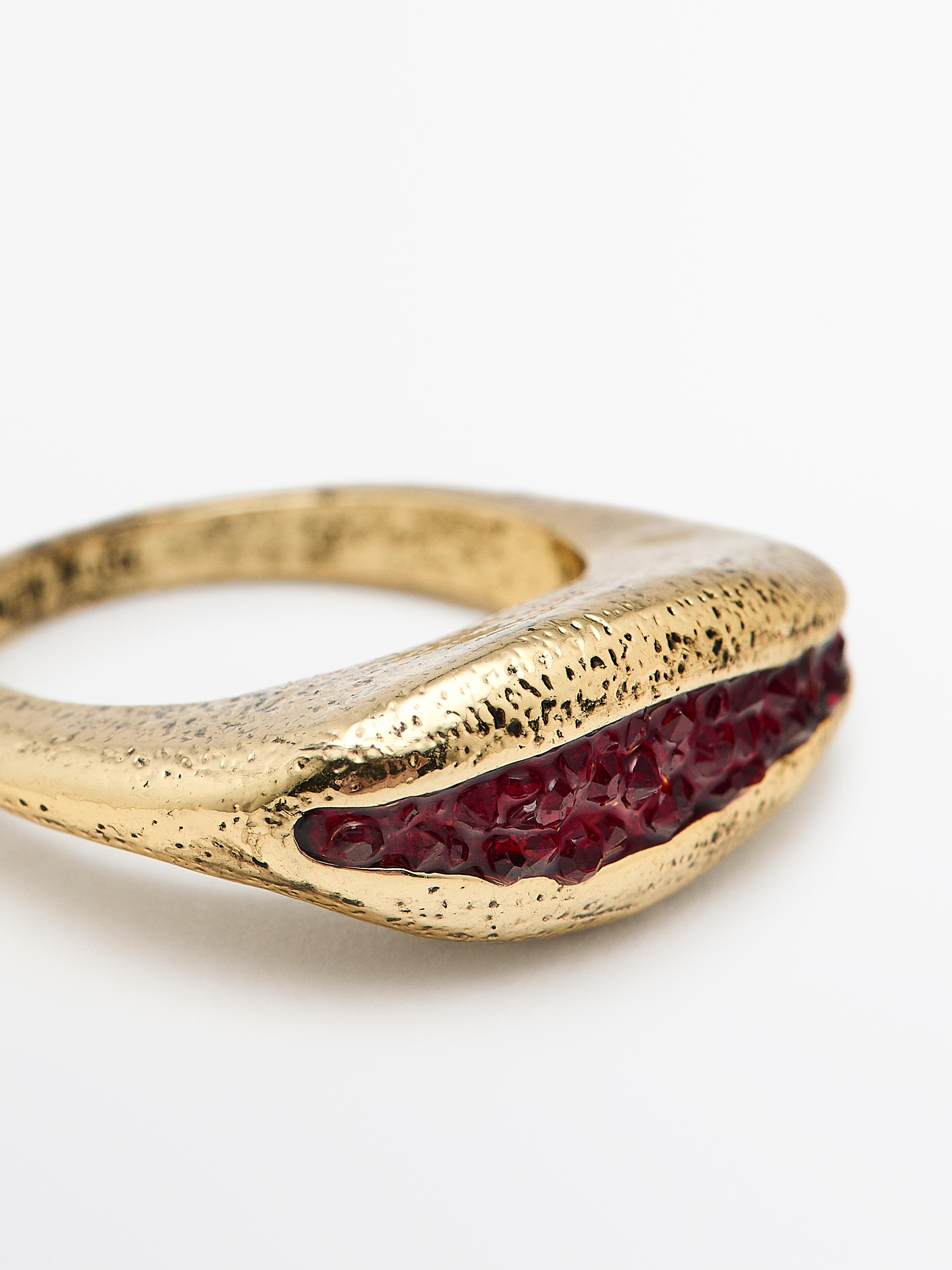 Close-up of a gold ring with an irregular design and a central red detail.