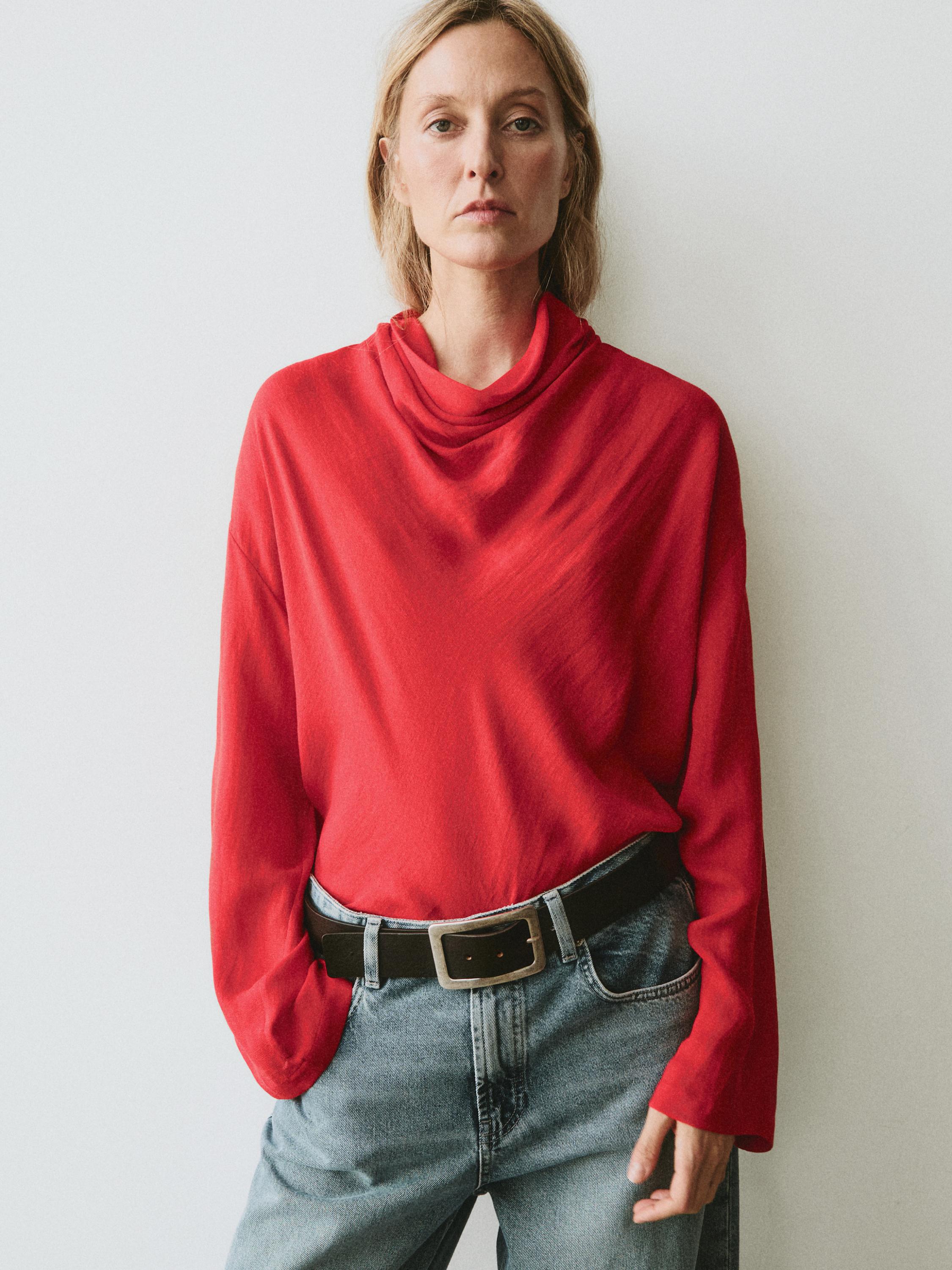 "Conxunto de blusa coral con colo drapeado e vaqueiros azuis con cinto negro."