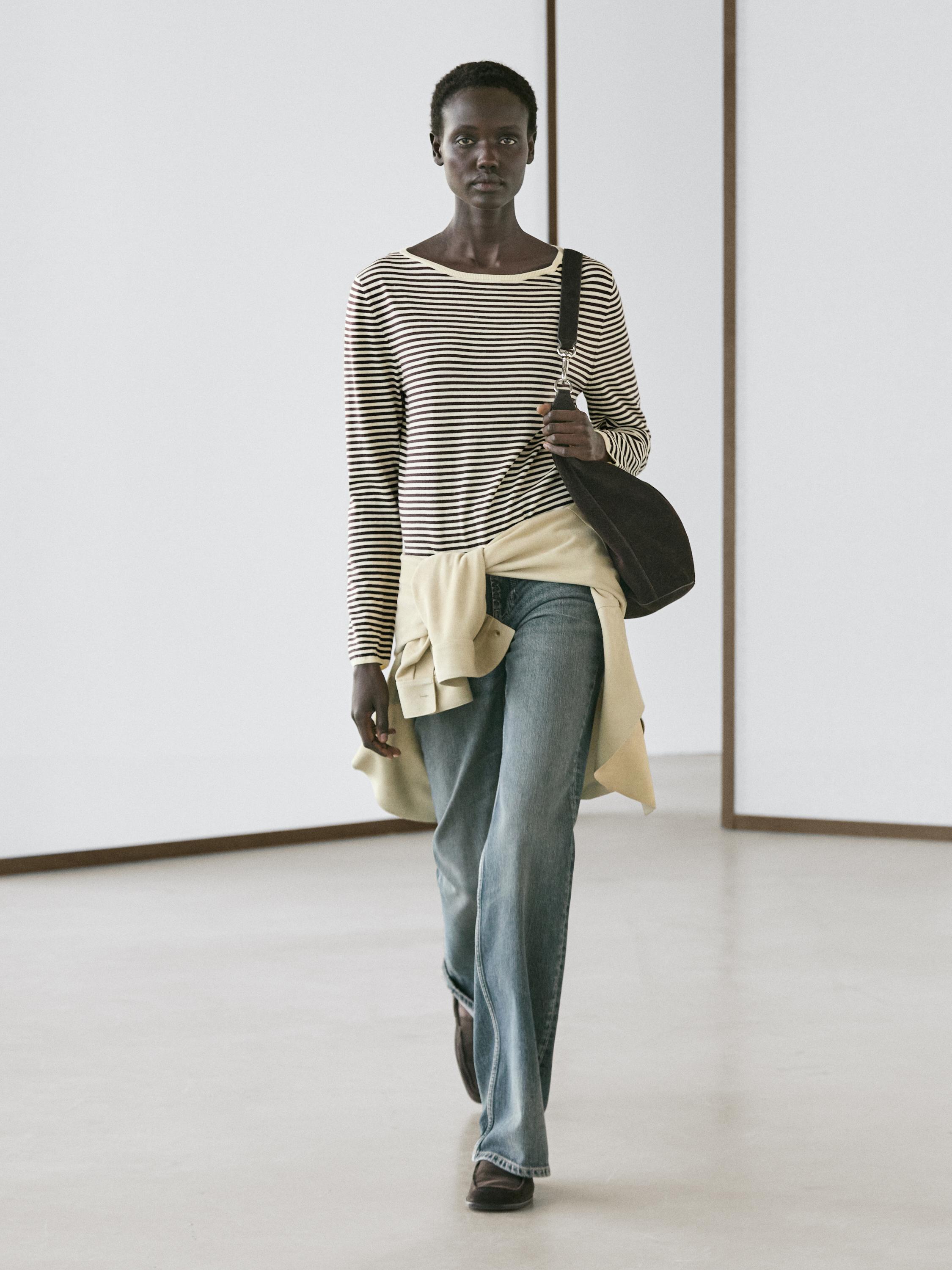 Conjunto de suéter de rayas crudo y negro, jeans azules acampanados y bolsa negra al hombro.