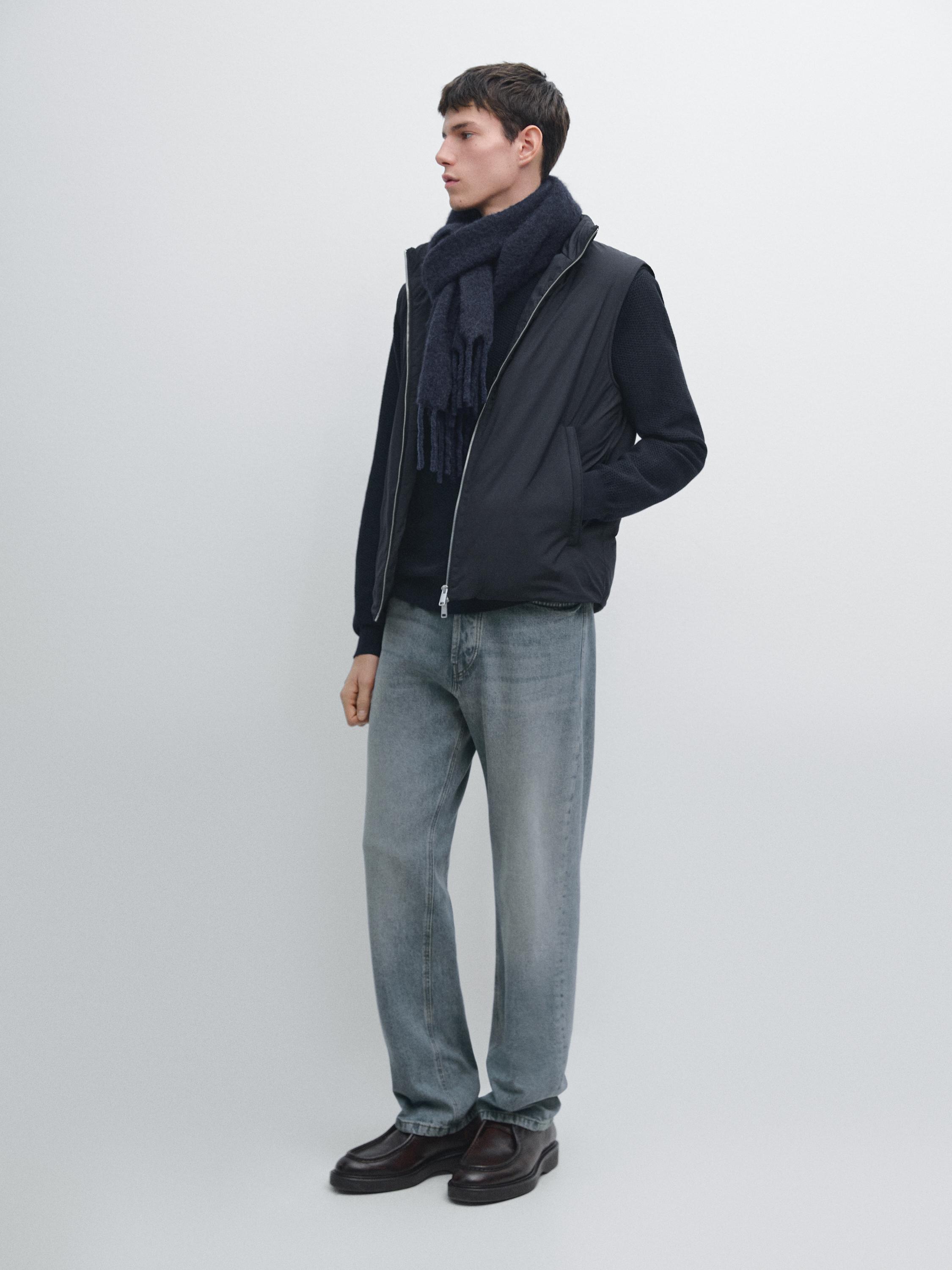 Completo con gilet blu navy con tasche laterali, maglione scuro, jeans chiari e scarpe marroni.