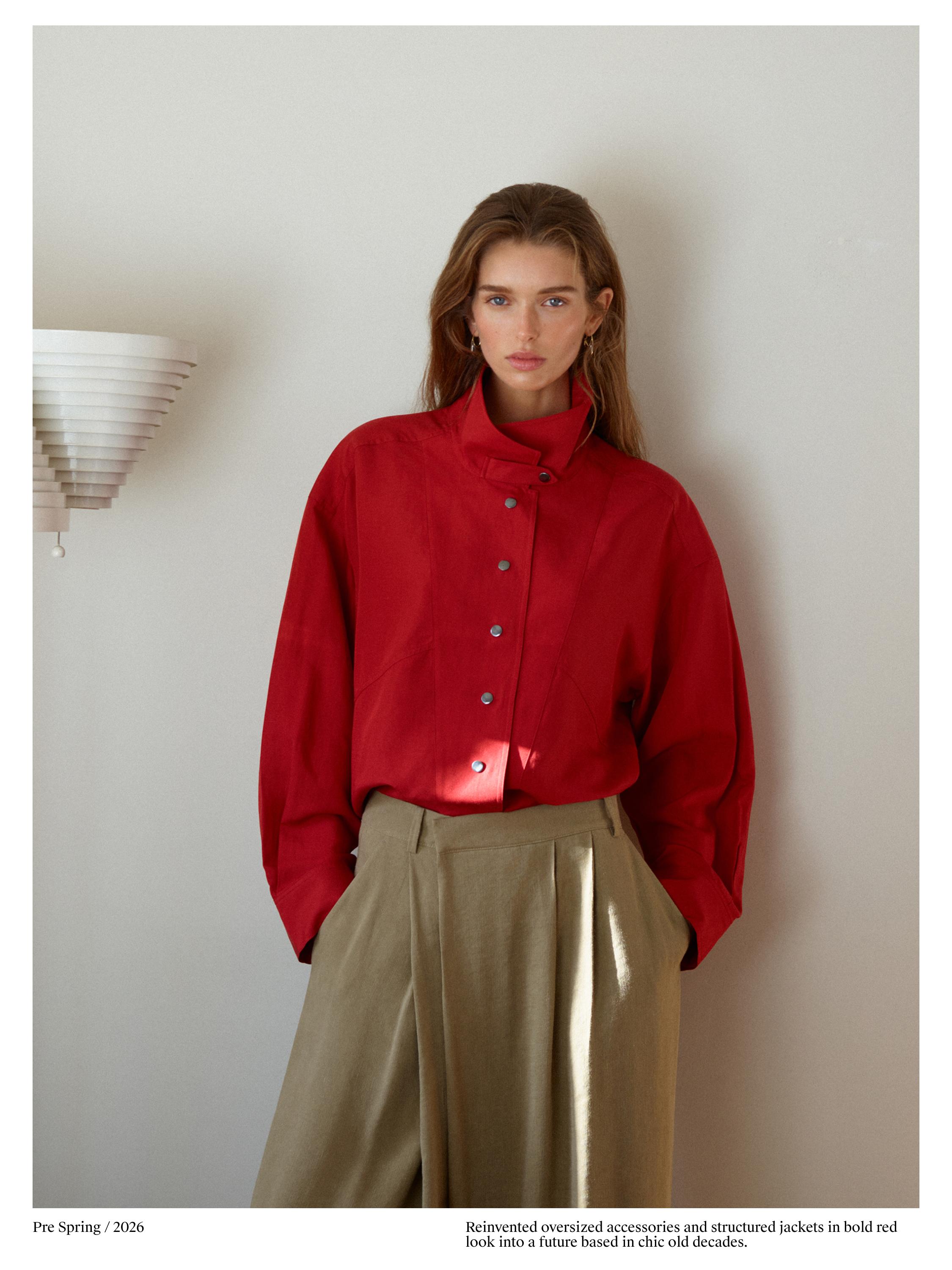 Комплет со црвена јакна со метални копчиња и беж панталони со висок струк со набори.