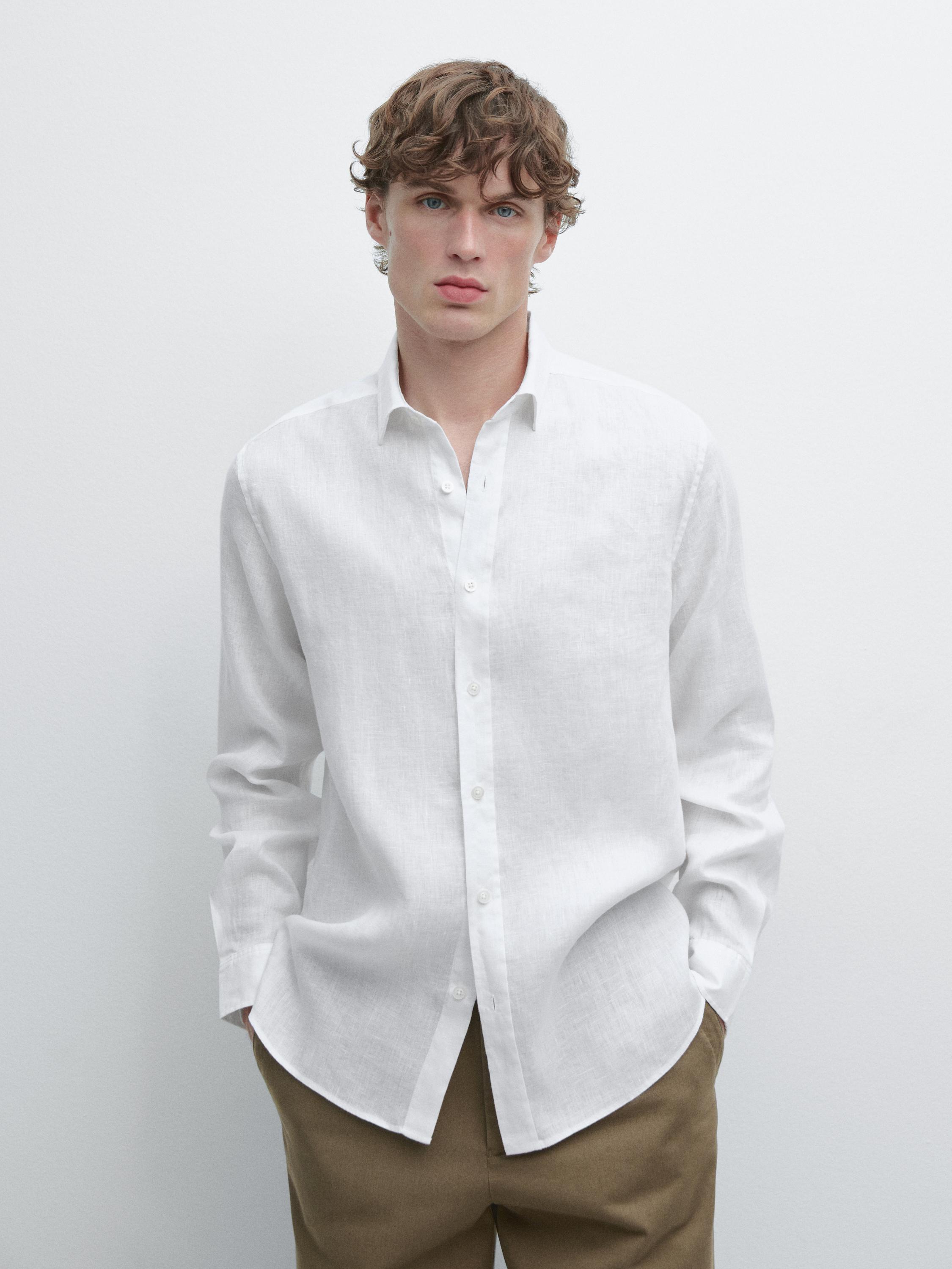 Conjunto de camisa branca de manga comprida com botões frontais e gola clássica, combinada com calças castanhas.