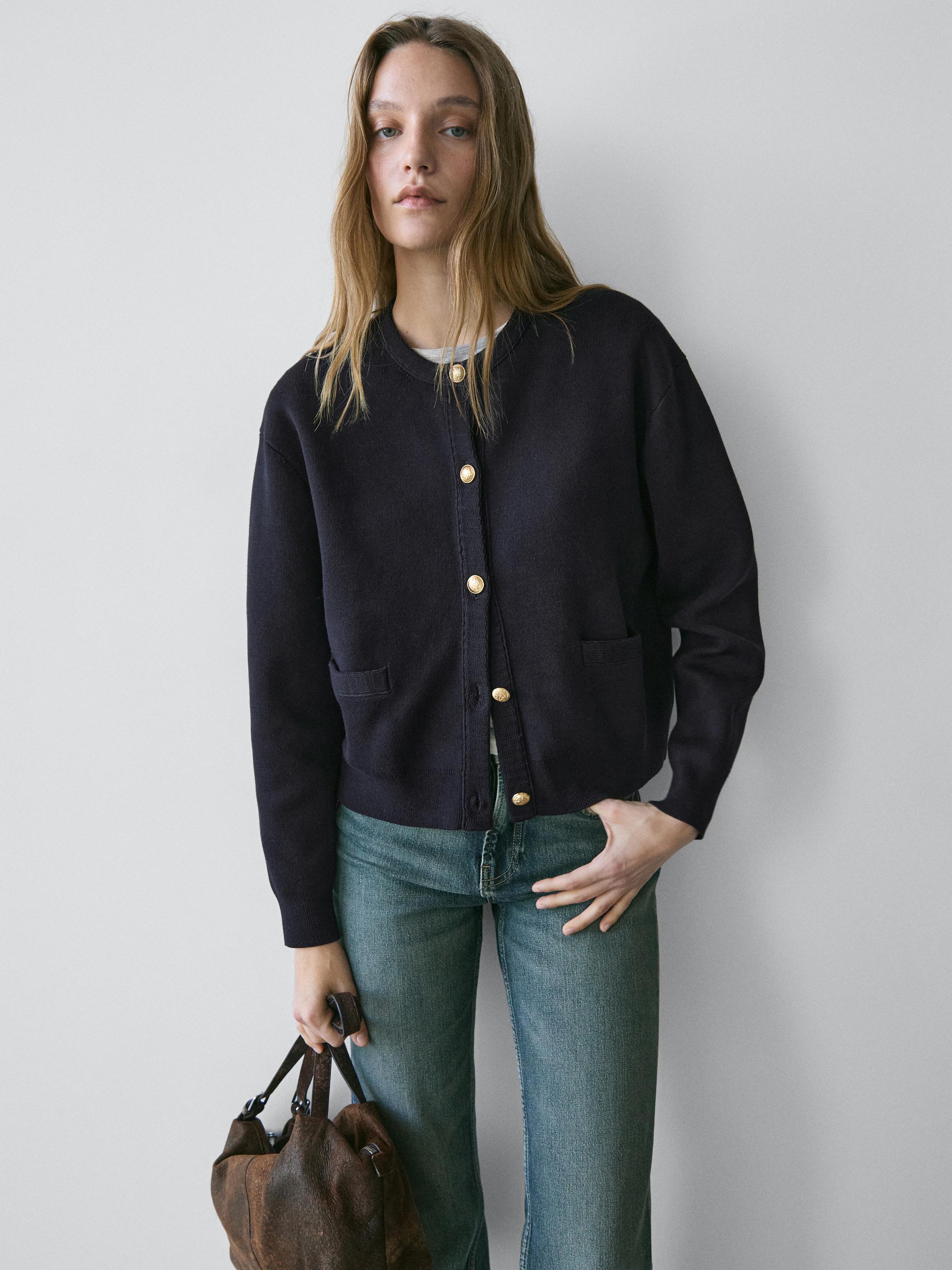 Conjunto de cárdigan azul marino con botones dorados y bolsillos frontales, combinado con jeans azules.