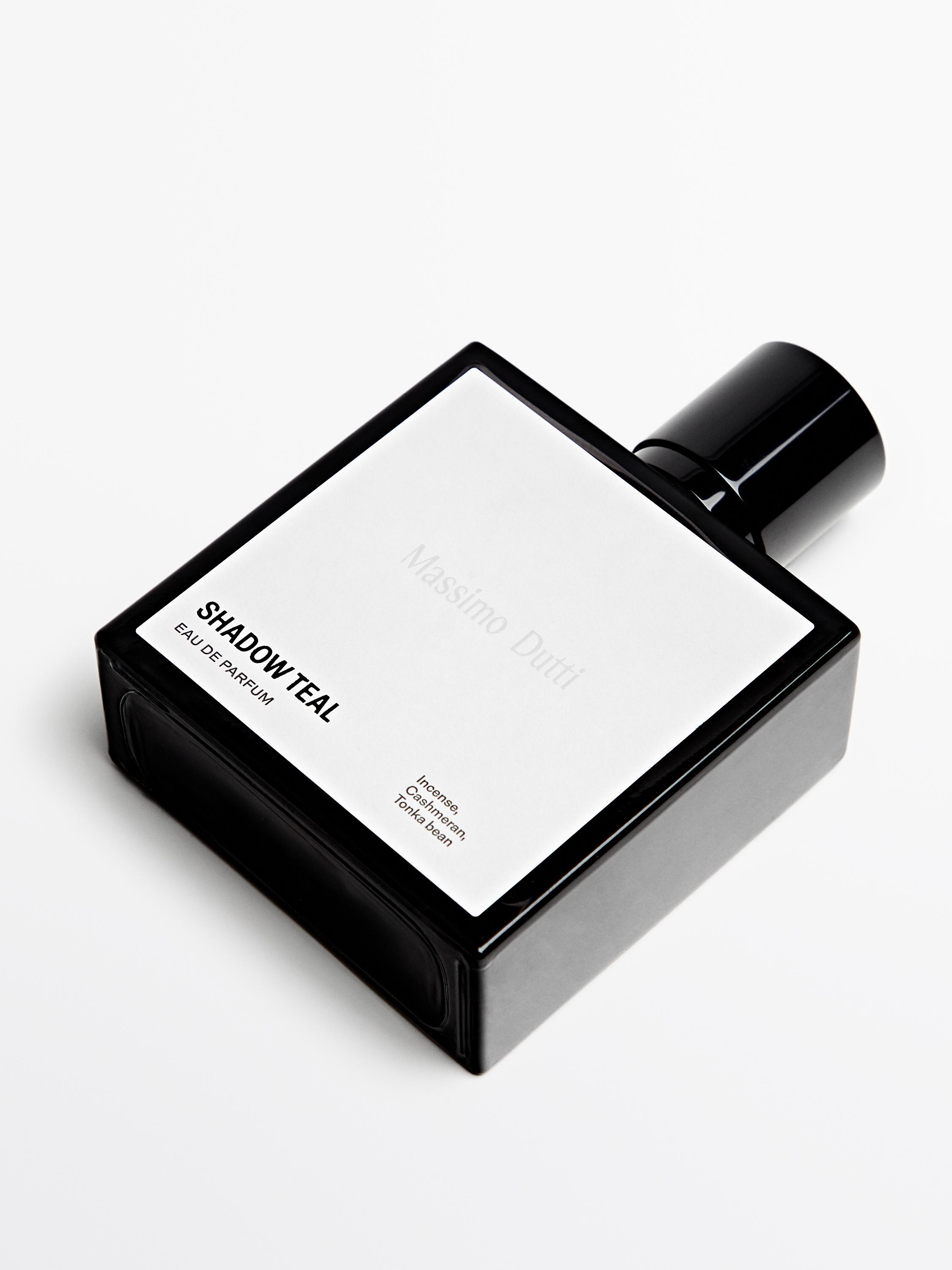 Botella de perfume negro con texto visible "SHADOW TEAL EAU DE PARFUM". Etiqueta blanca con detalles de incienso y haba tonka.