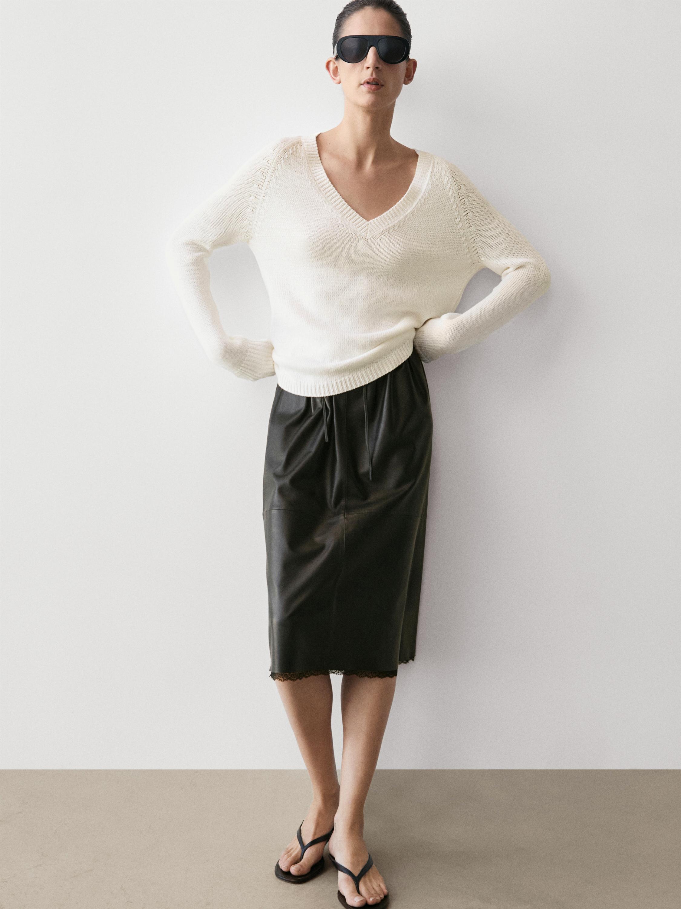 Witte V-hals trui en zwarte midi-rok met kanten detail aan de zoom.
