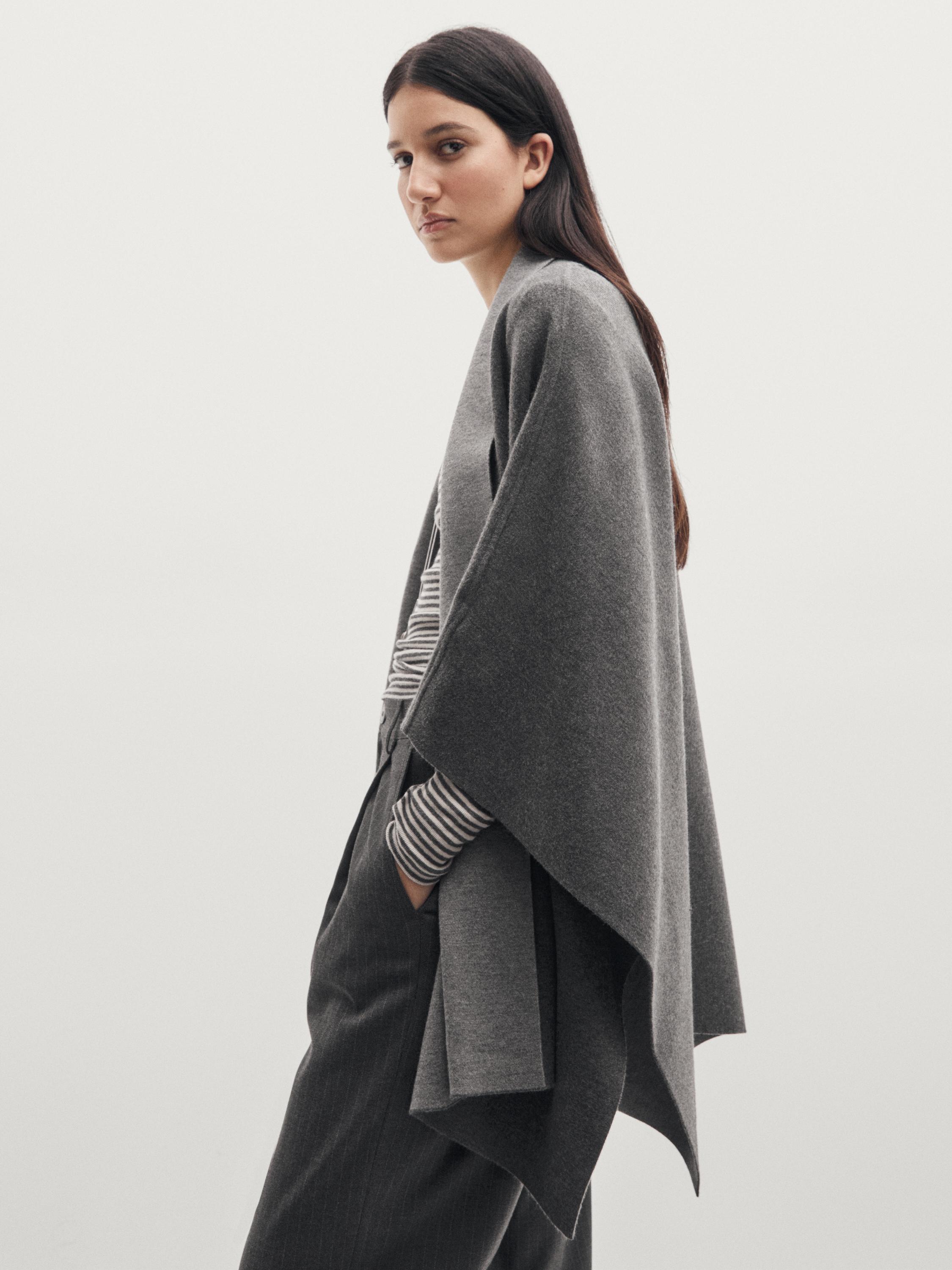 Ensemble de cape grise en maille sur t-shirt rayé et pantalon gris.