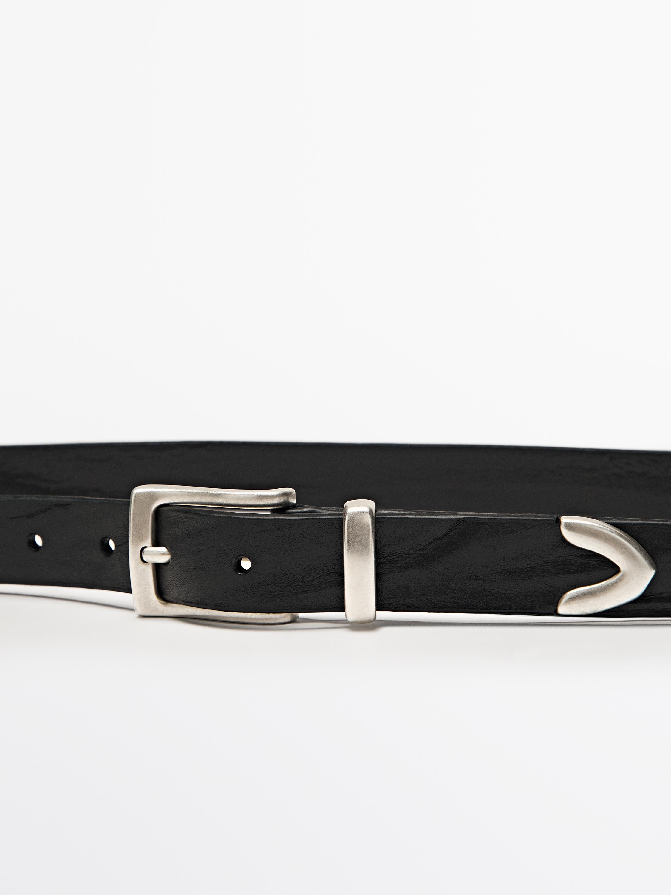 Détail de ceinture noire avec boucle métallique et embout décoratif.