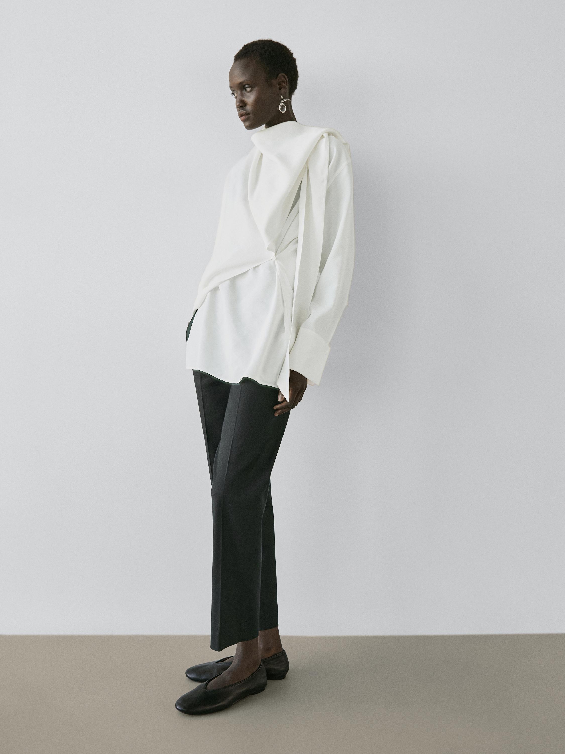 Ensemble blouse écrue à détail drapé et pantalon droit noir.