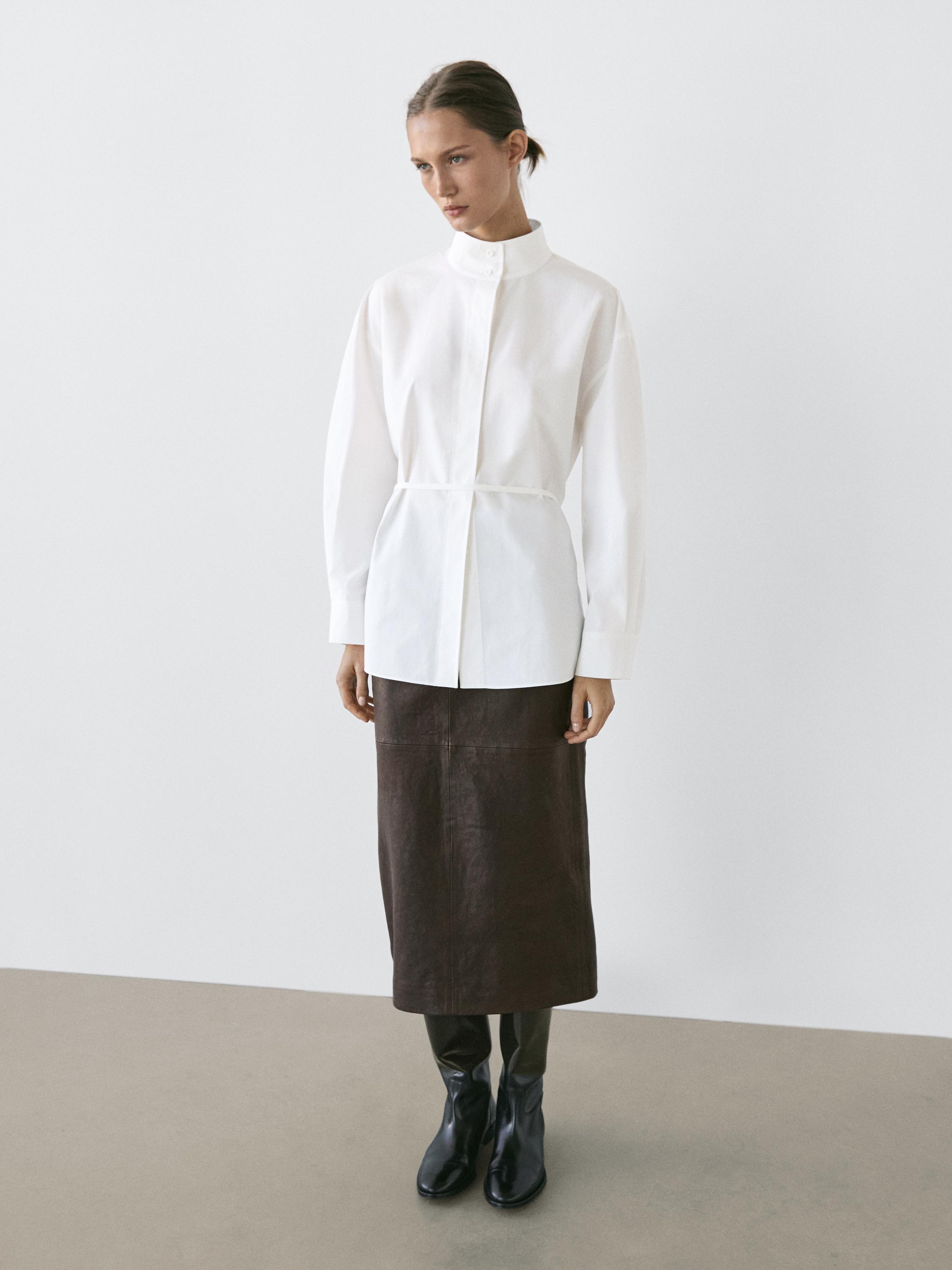 Ensemble de chemise blanche à col roulé avec ruban et jupe longue marron, bottes noires.