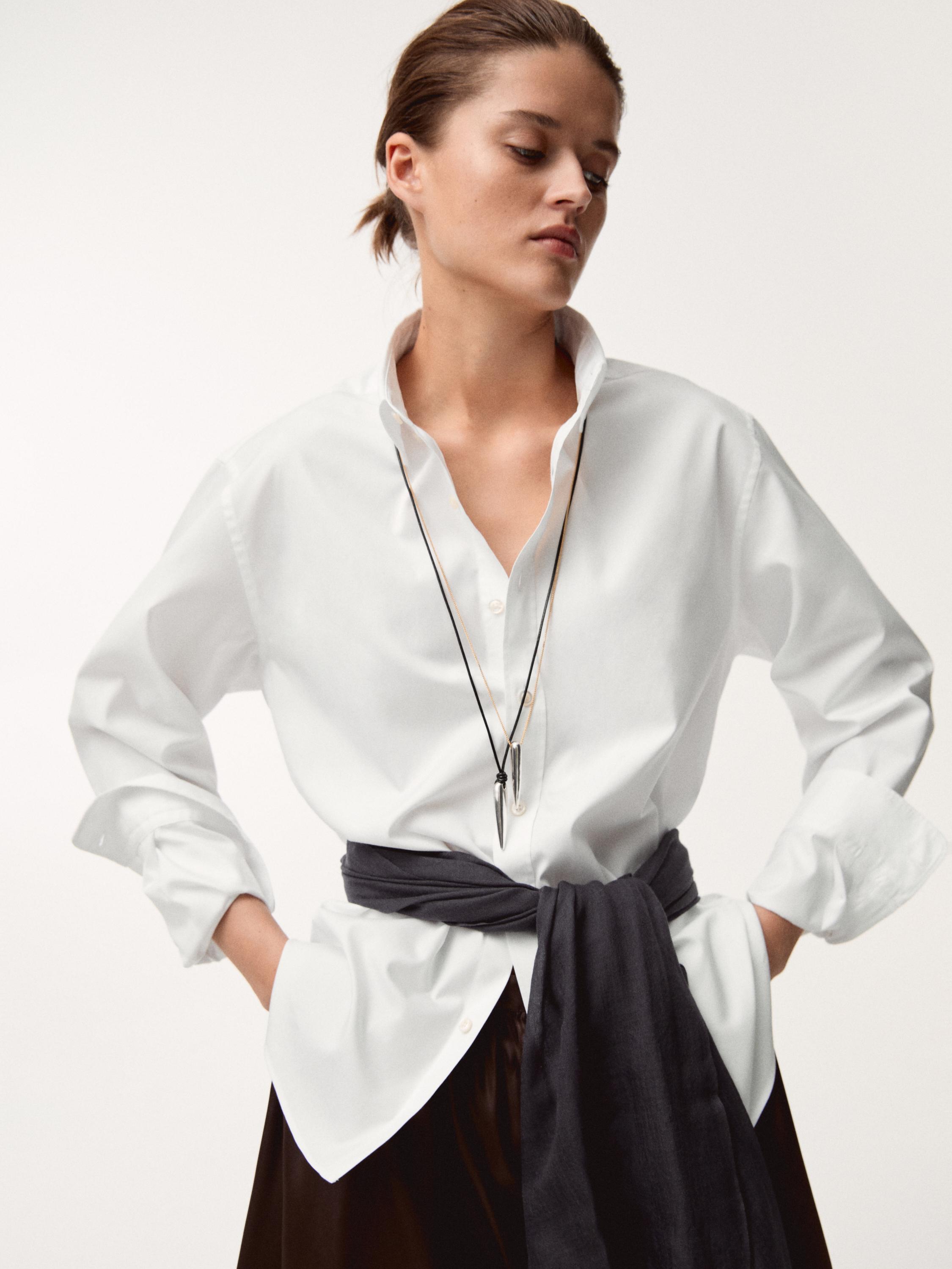 Conjunto de camisa blanca con colgante de péndulo plata y pañuelo negro atado a la cintura.