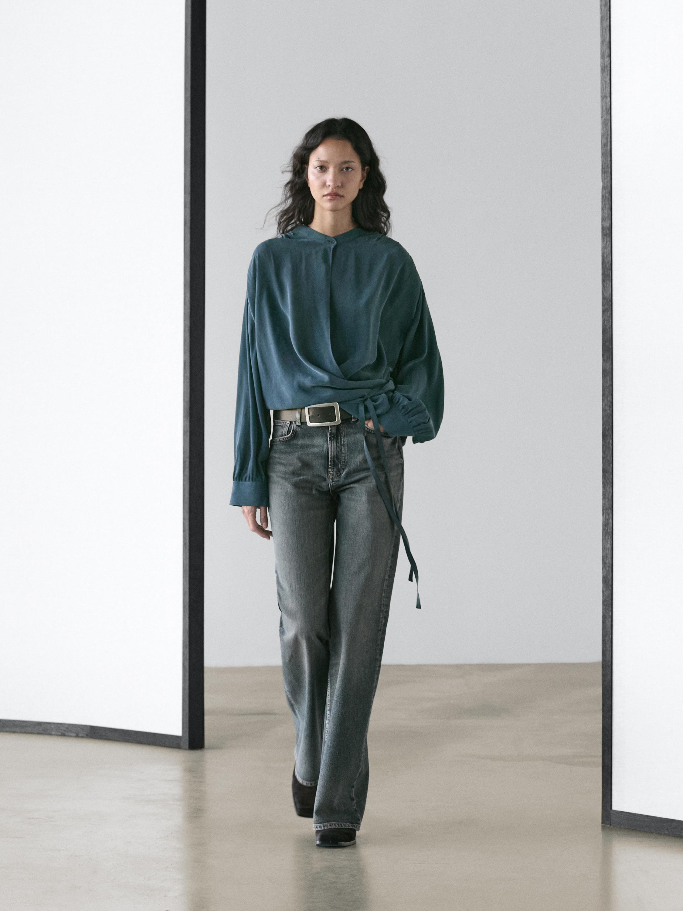 Set aus fließender, überlappender grüner Bluse mit Taillenband und gerader grauer Jeans.