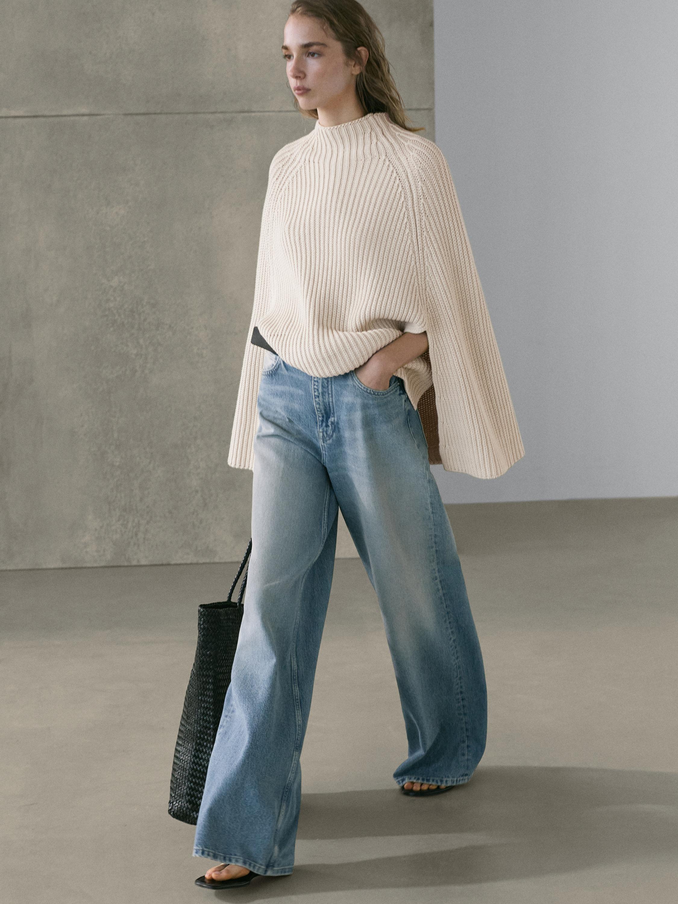 Lyseblå, højtaljede, vide jeans med beige striktrøje og sort taske.