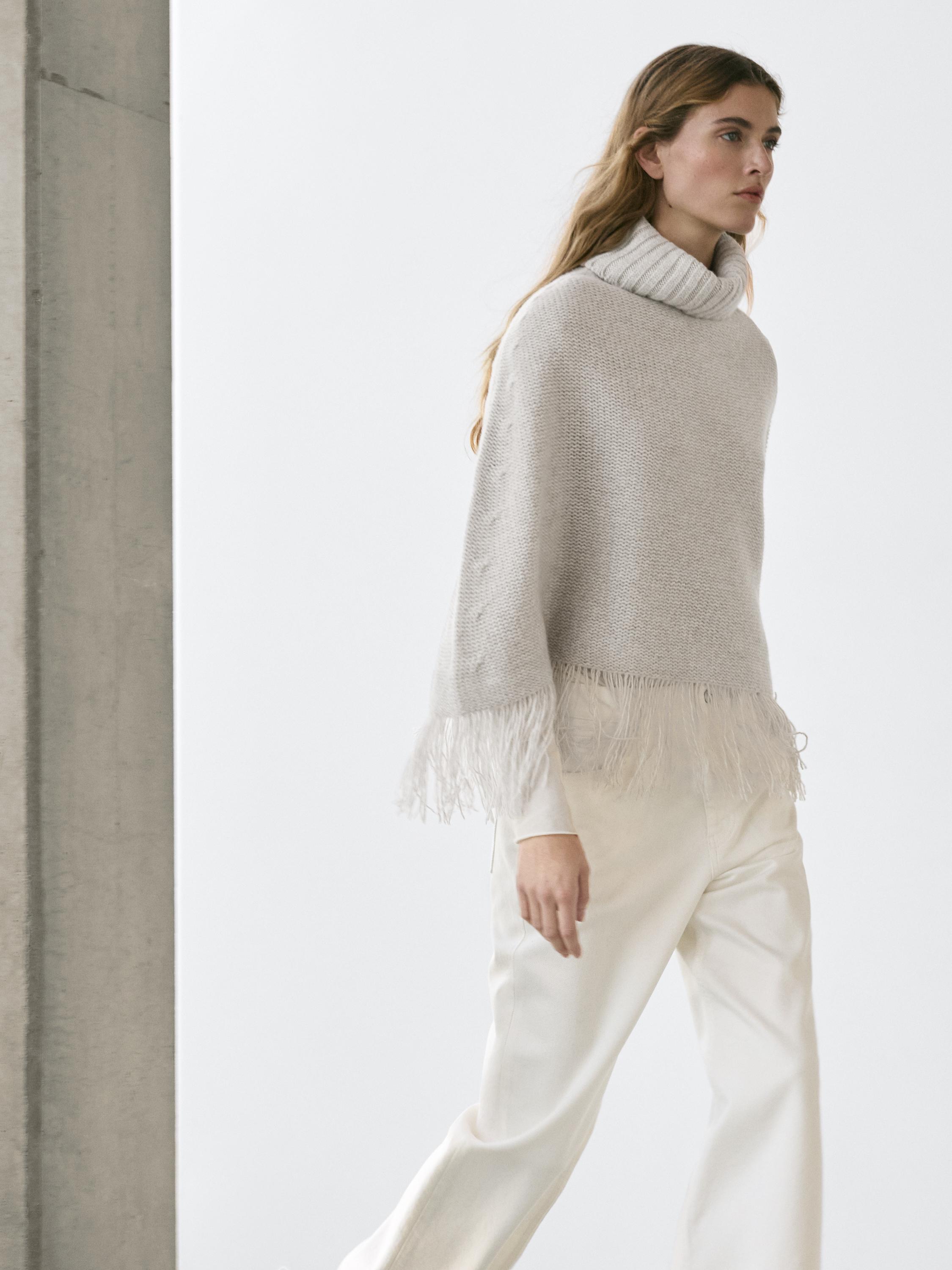 Gray turtleneck sweater set with fringe hem, paired with straight white pants.