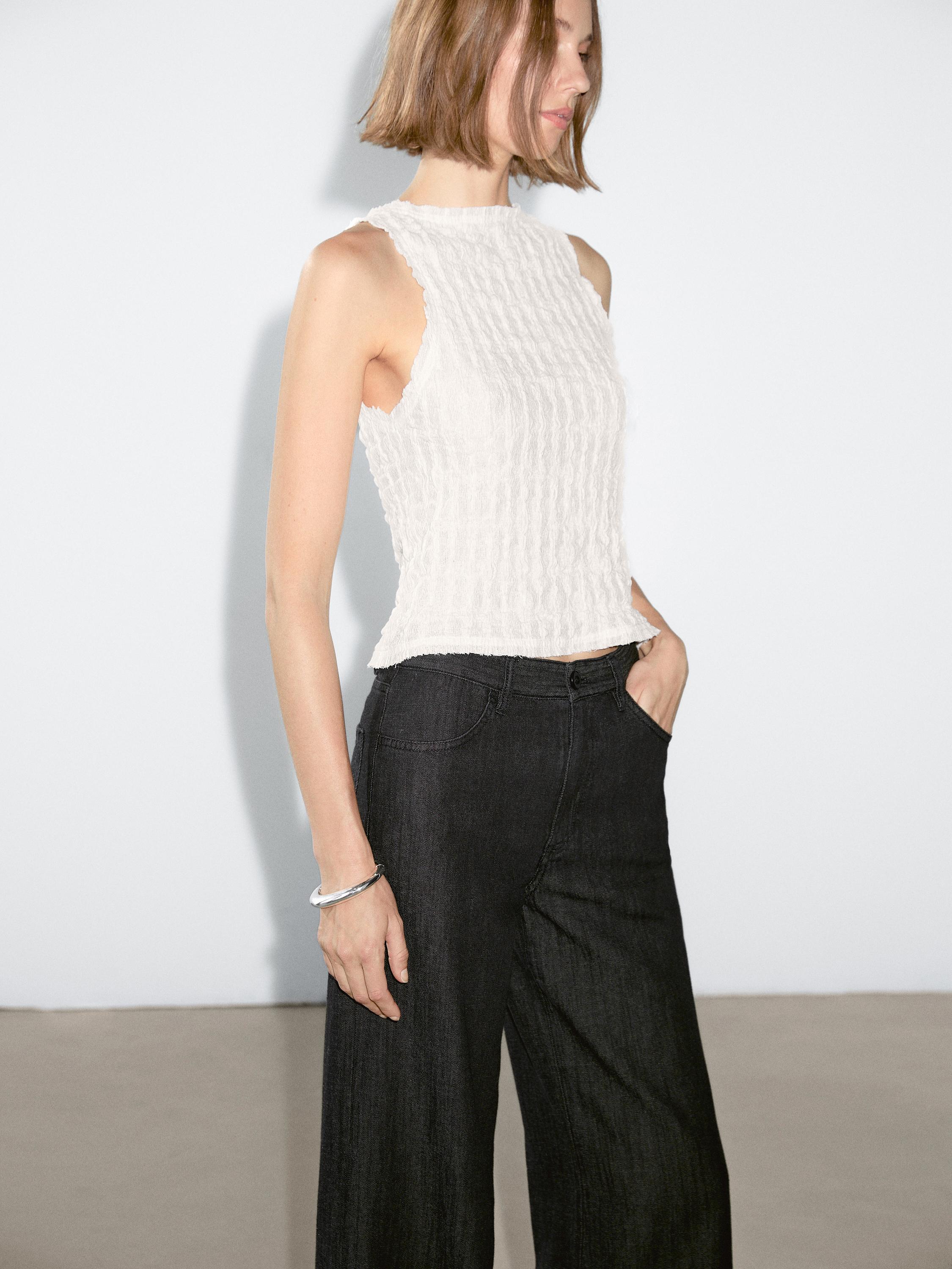 Plan moyen d'un jean foncé avec des poches avant et un chemisier blanc texturé sans manches.