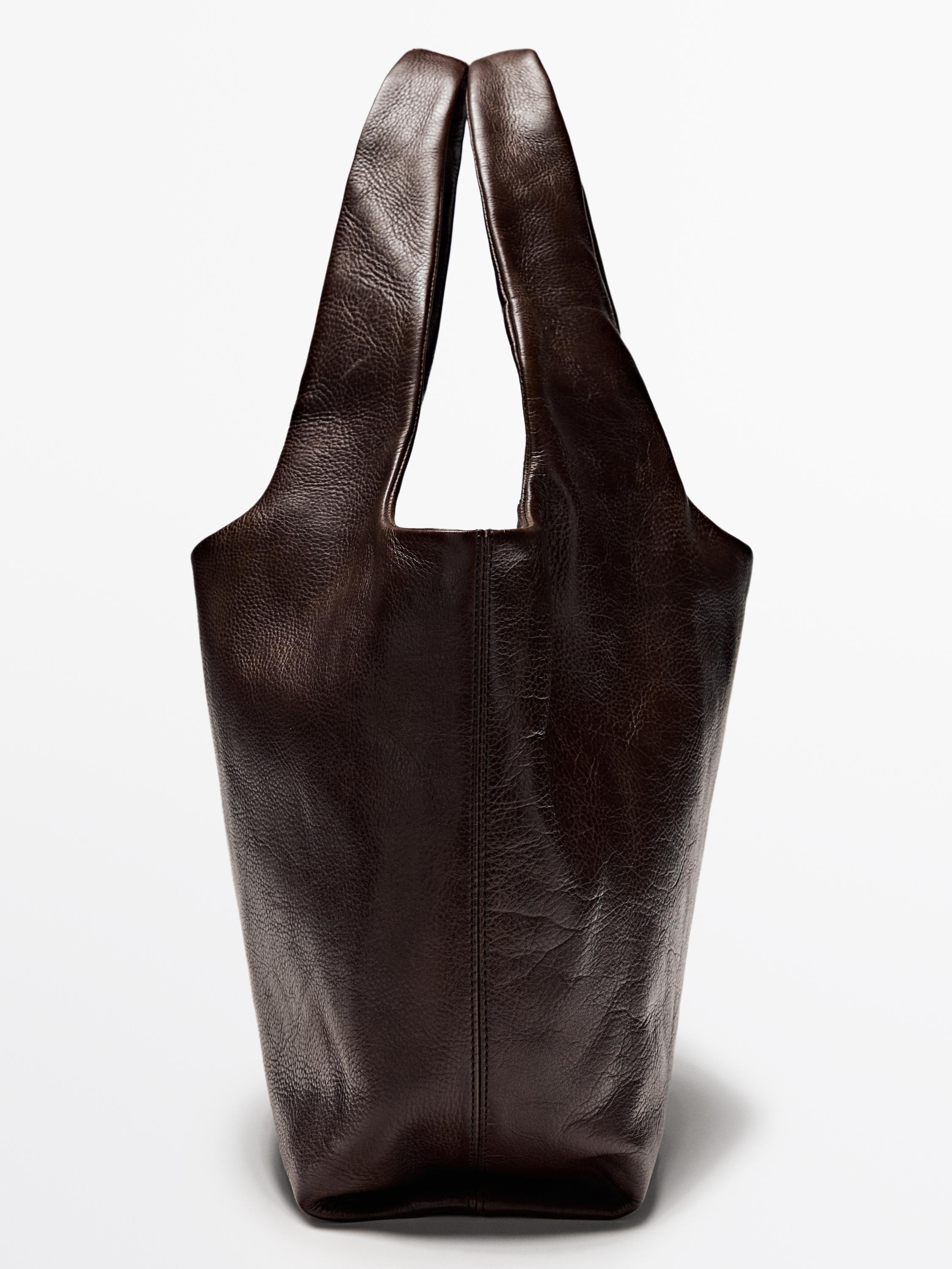 Tampilan depan tas tangan cokelat dengan tali lebar dan jahitan vertikal di bagian tengah.