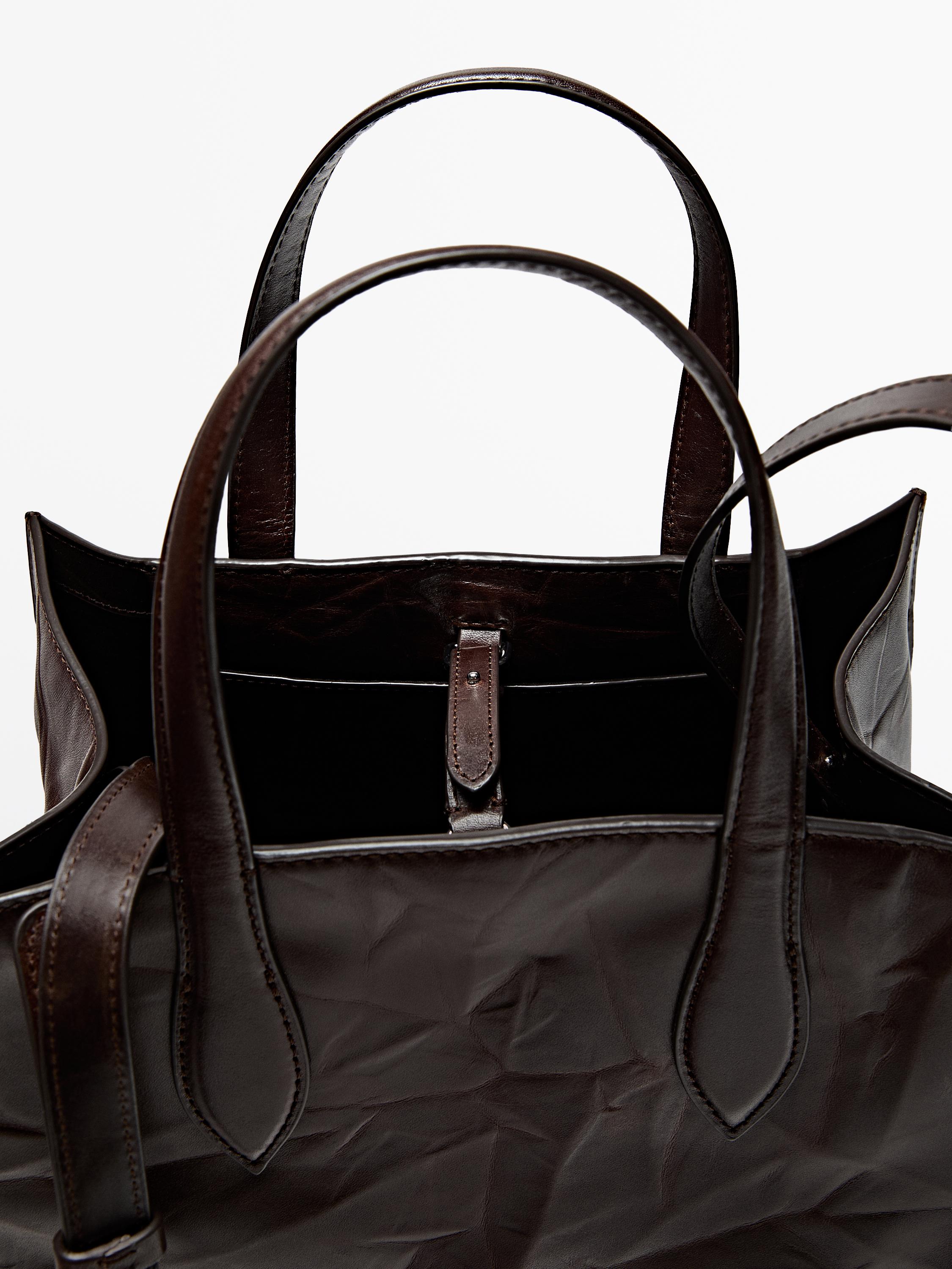 Detalle de bolso marrón con asas dobres e peche de lingüeta. Interior amplo visible.