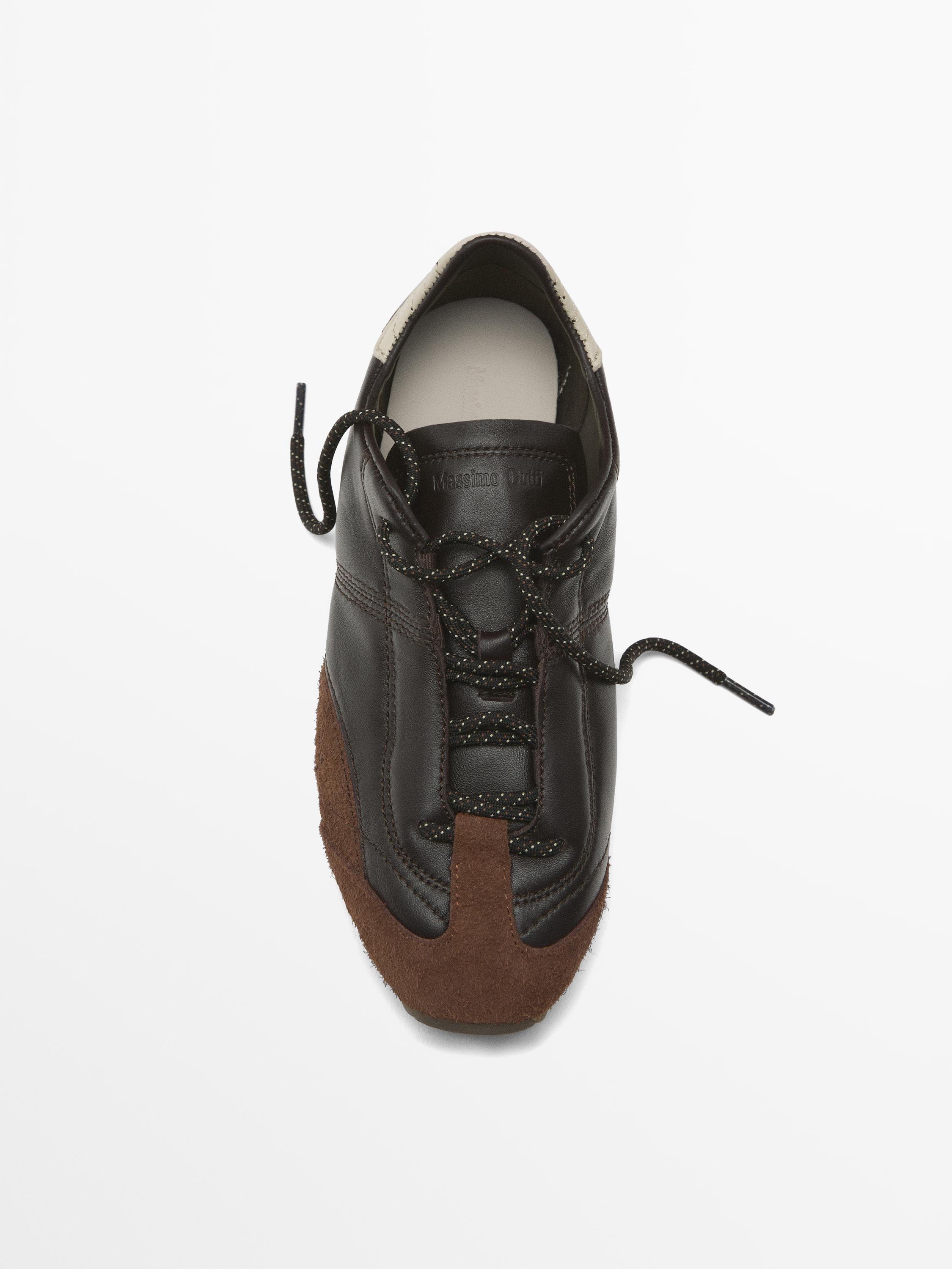 منظر من الأعلى لحذاء بني غامق اللون برباط أسود وتفاصيل من جلد الغزال البني.