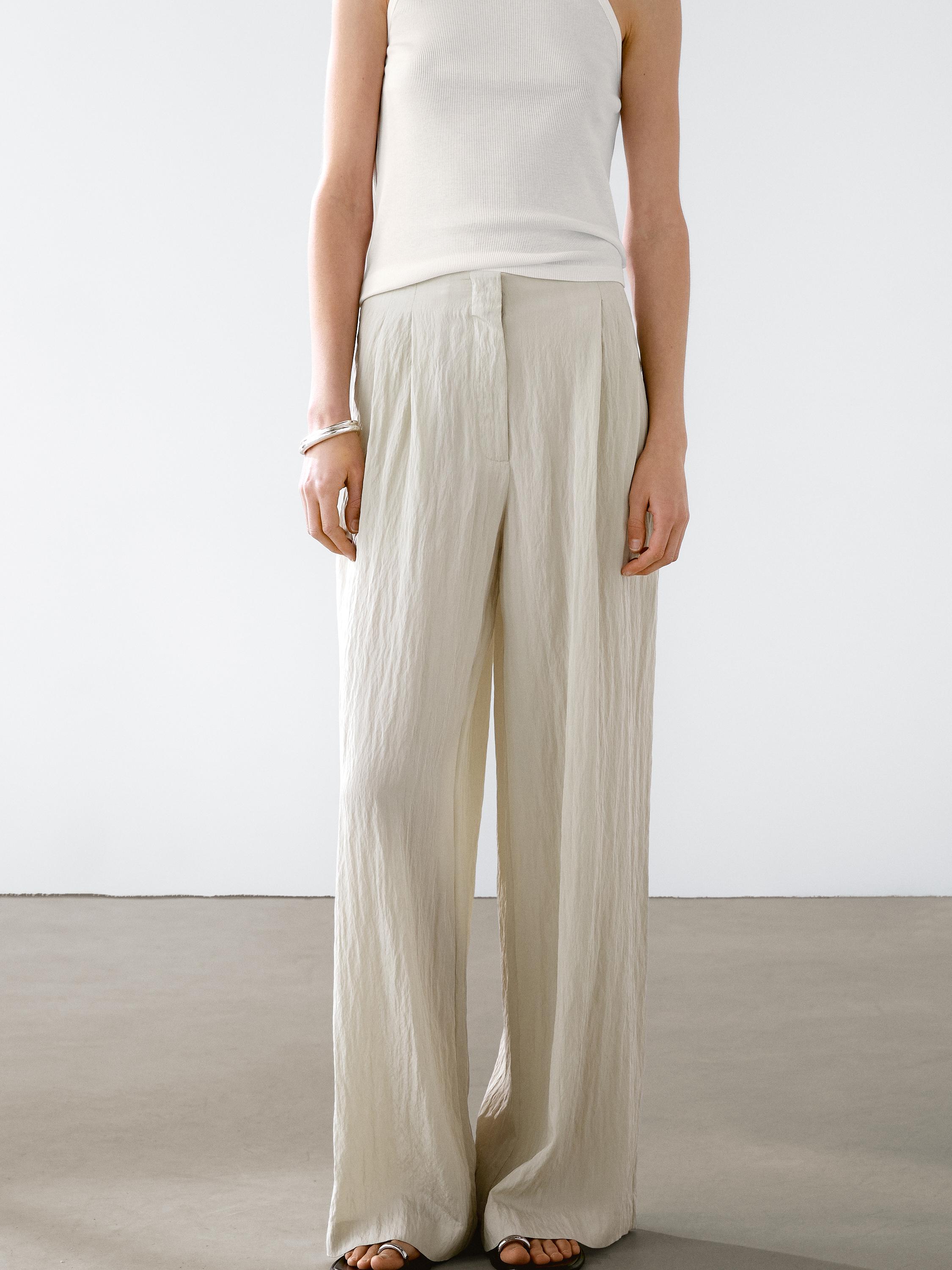 Ensemble pantalon beige à jambes larges et pinces avec un haut blanc sans manches.