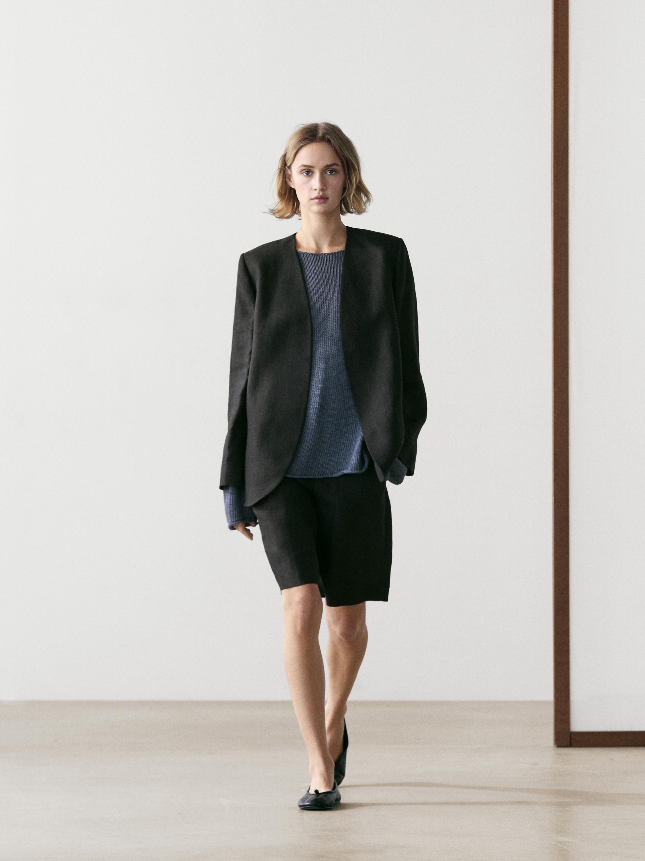 Conjunto de blazer negro sin solapa, suéter azul y bermudas negras.