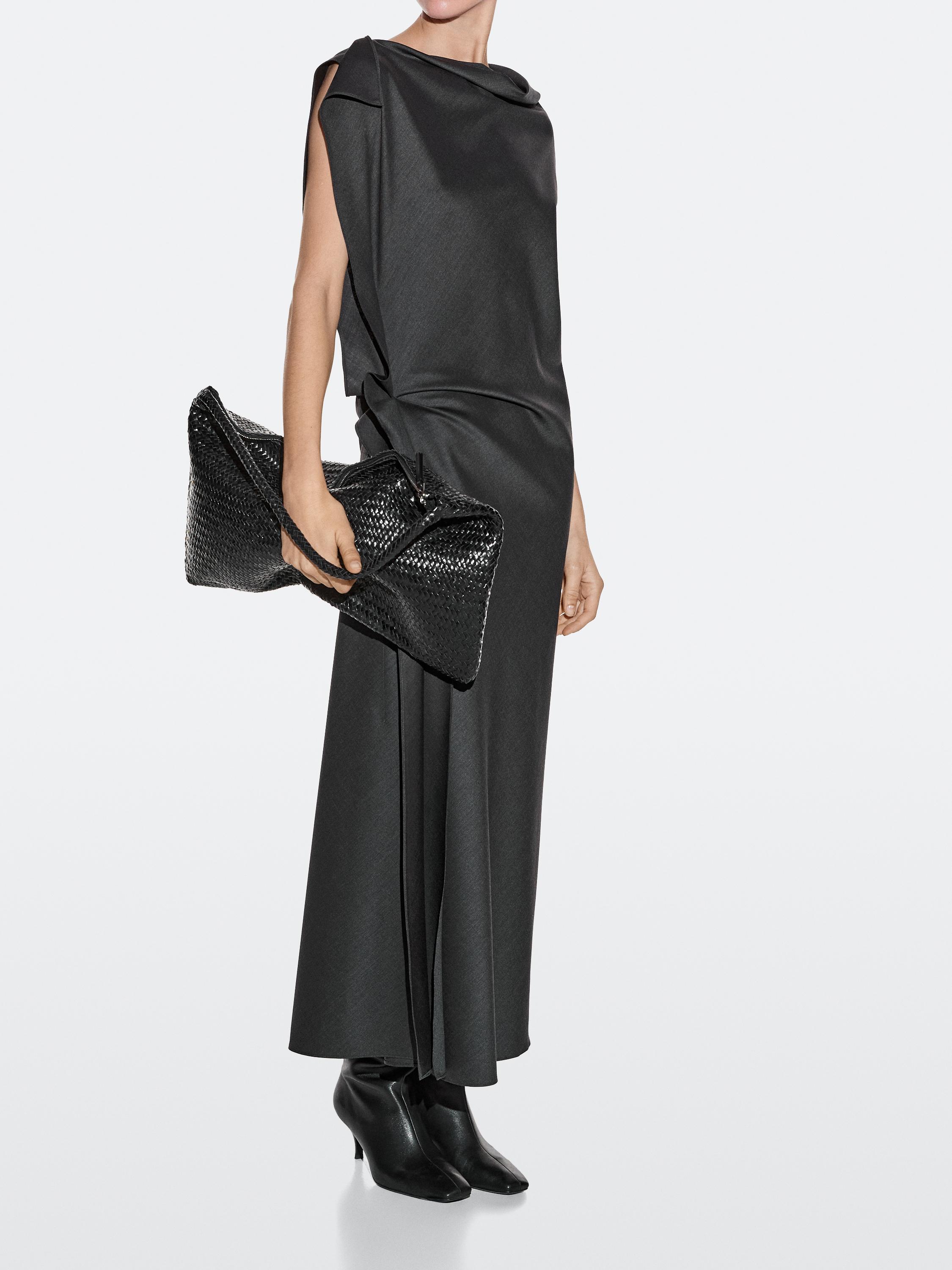 Conjunto de vestido negro sin mangas y botas negras, con bolso negro tejido en mano.