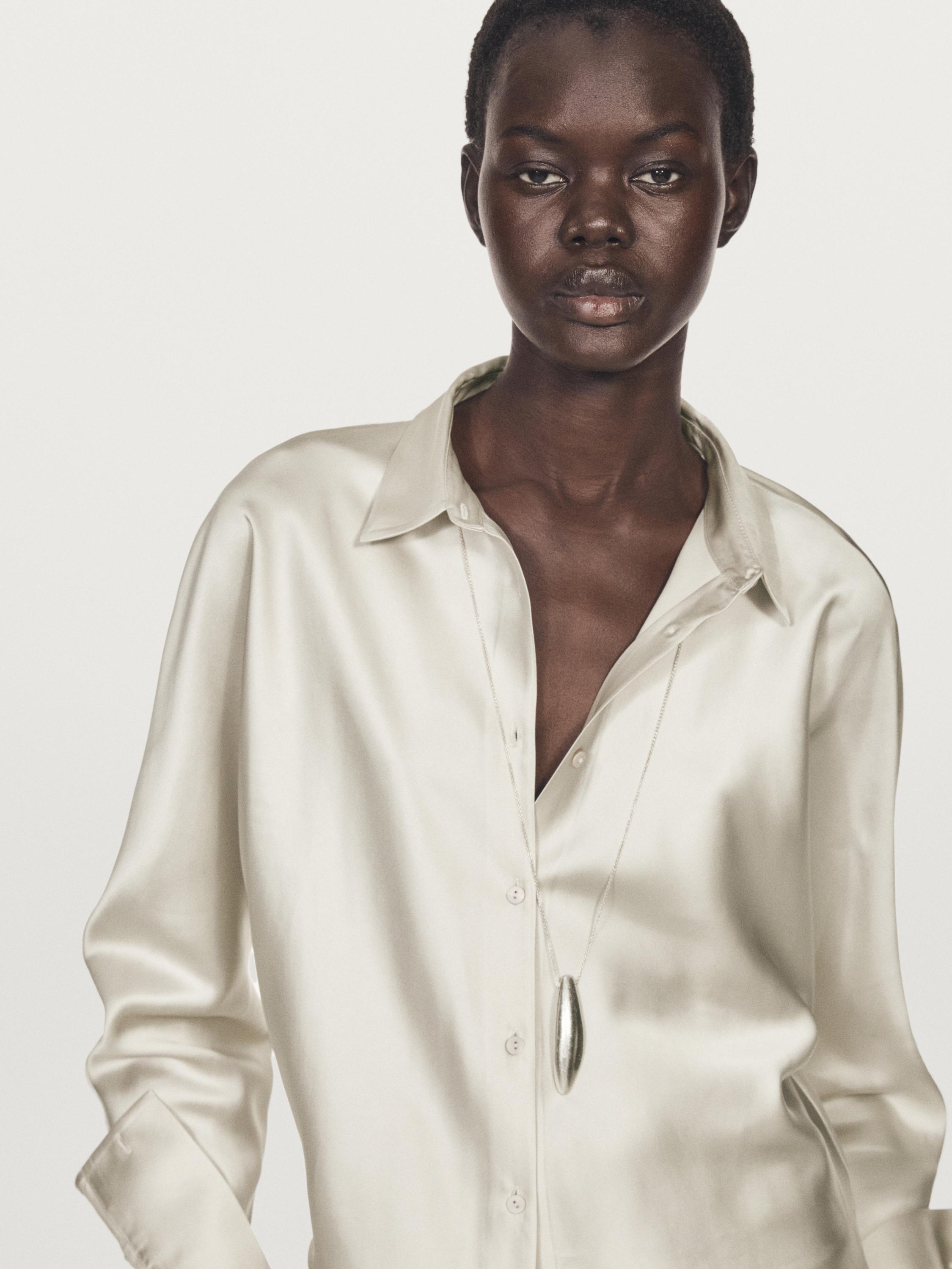 Крупный план серебряной атласной рубашки с рукавами «летучая мышь» и передней планкой.