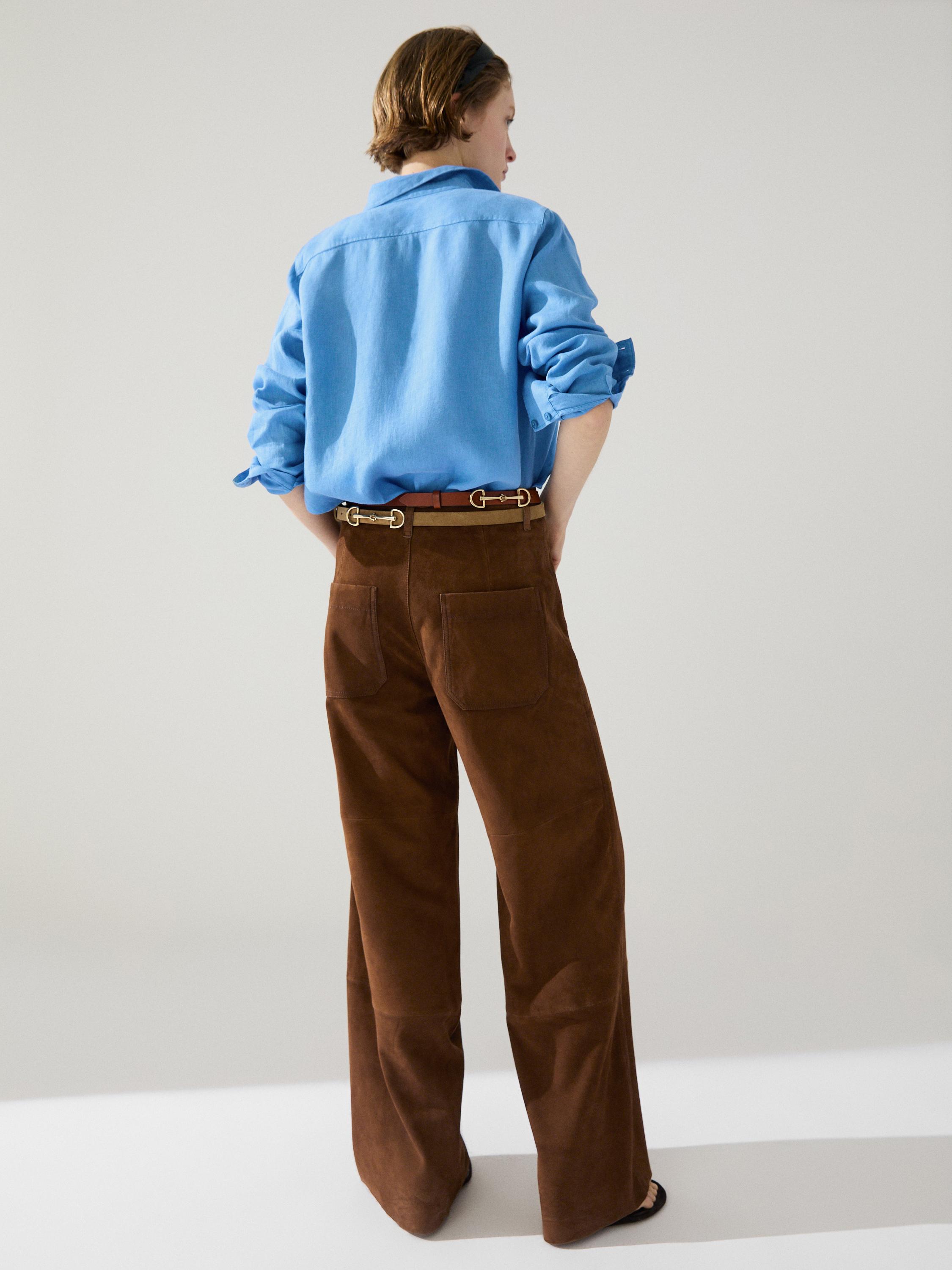 Conjunto de camisa azul con mangas dobladas y pantalones marrones de pierna ancha con bolsillos traseros.