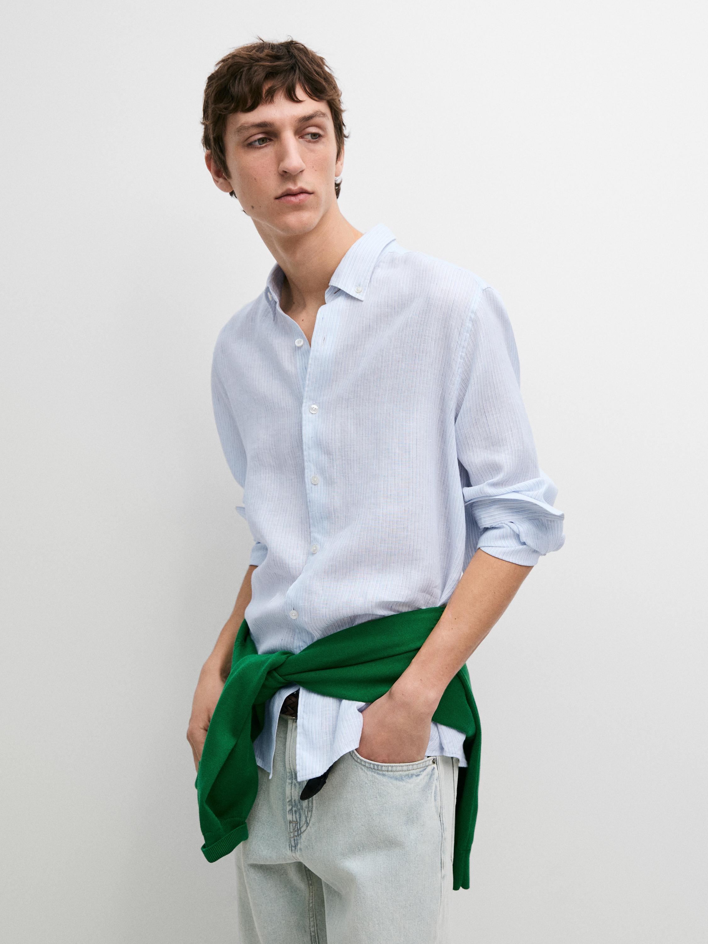 Hellblaues Langarmhemd mit Knöpfen und hellblaue Jeans. Grüner Pullover um die Taille gebunden.