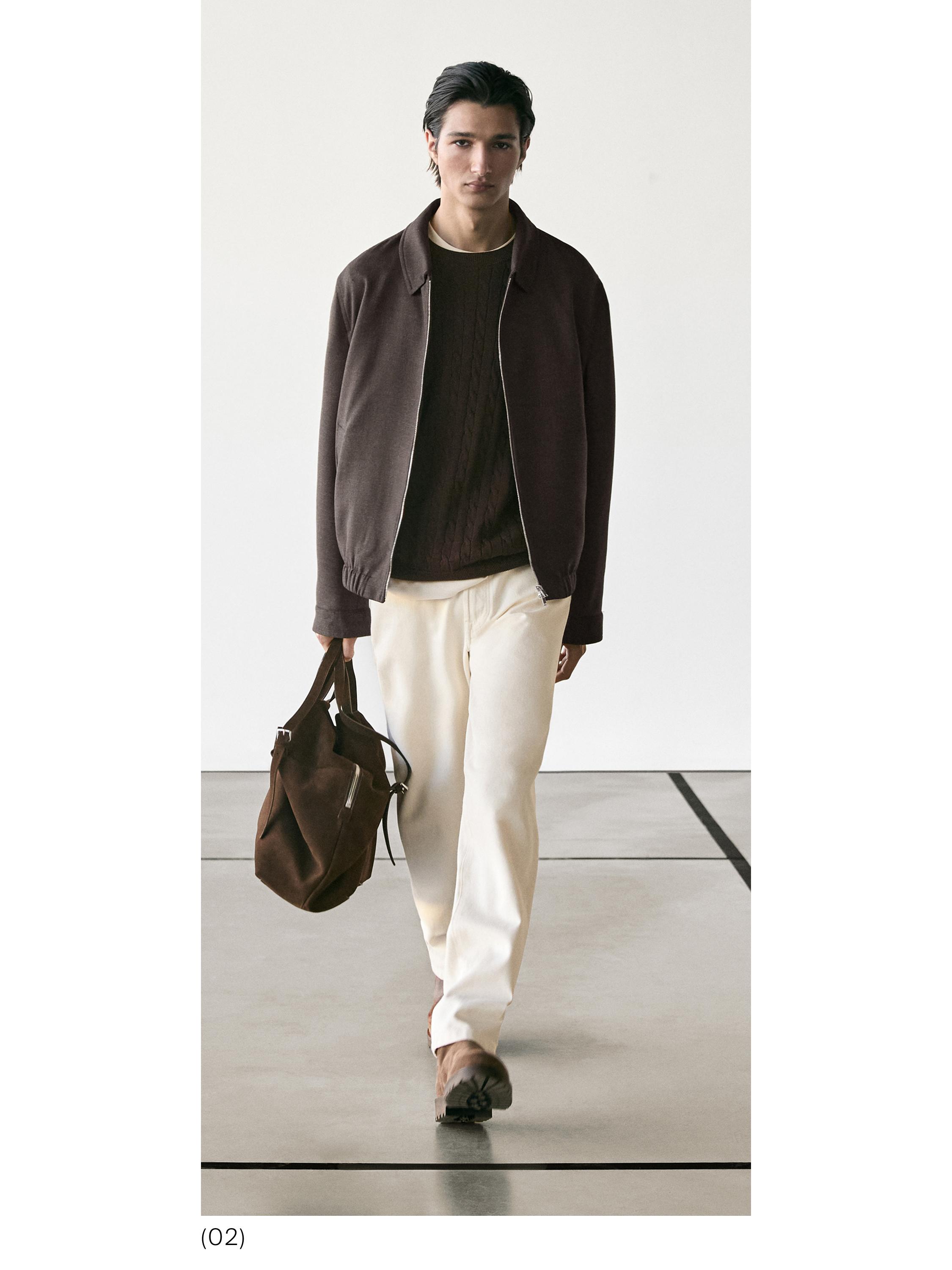 Apģērbs sastāv no brūnas jakas, tumša džempera, smilškrāsas biksēm un brūnām kurpēm. Kreisajā rokā viņam ir brūna soma.