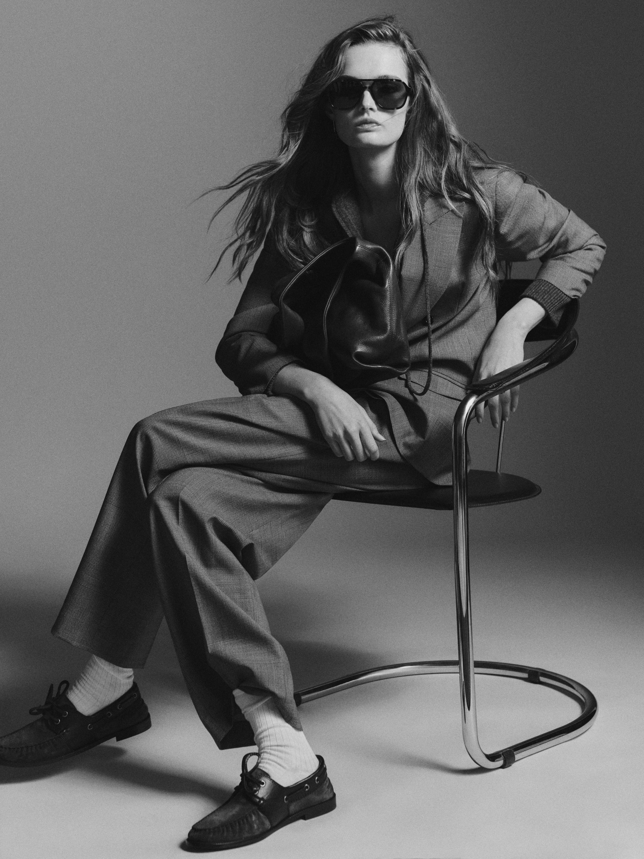 Pilkas kostiumas su atlapų švarku ir plačiomis kelnėmis. Matomi tamsūs batai ir šviesios kojinės.