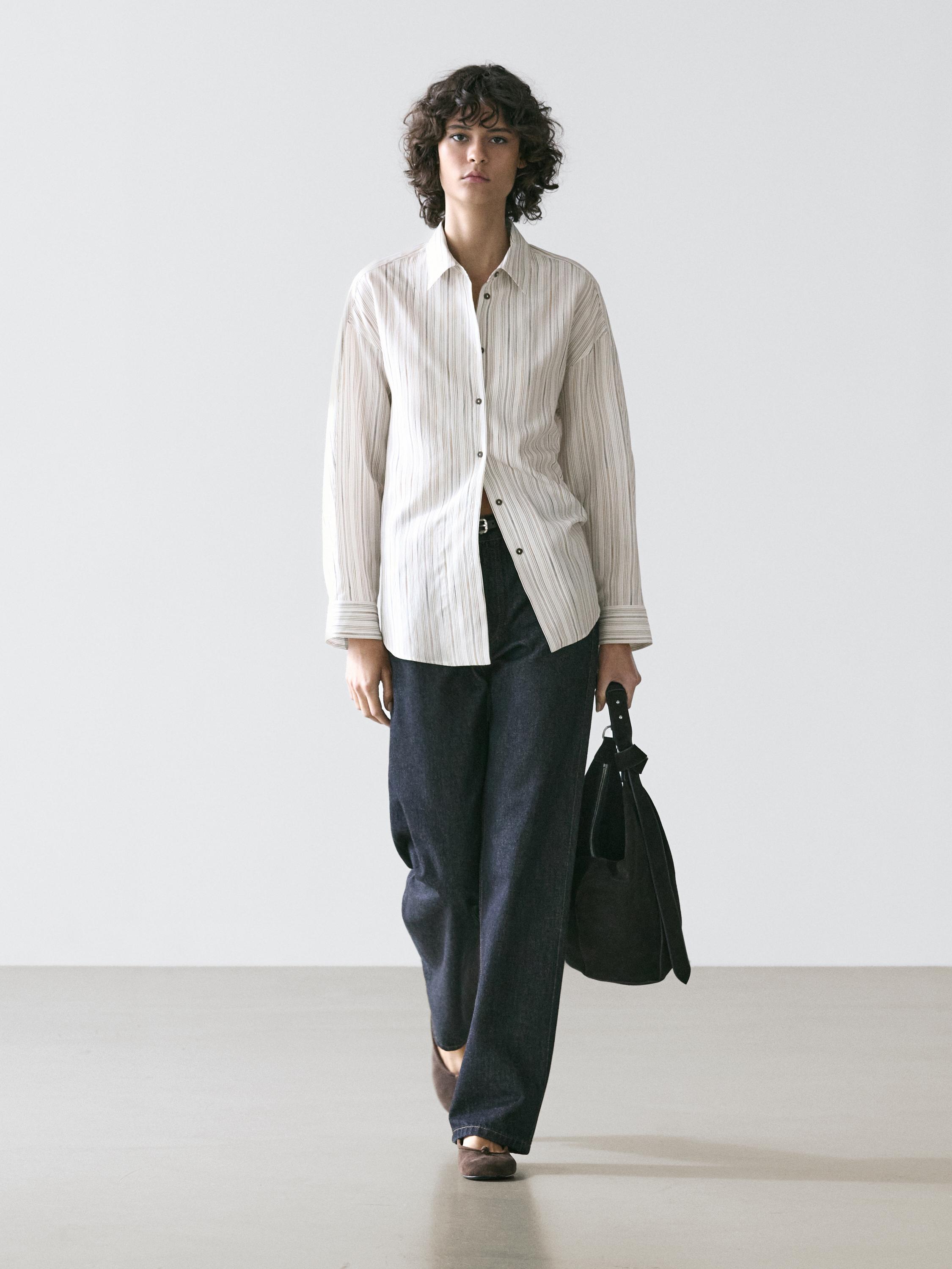 Conjunto de camisa blanca a rayas con botones y pantalones oscuros de pierna ancha.