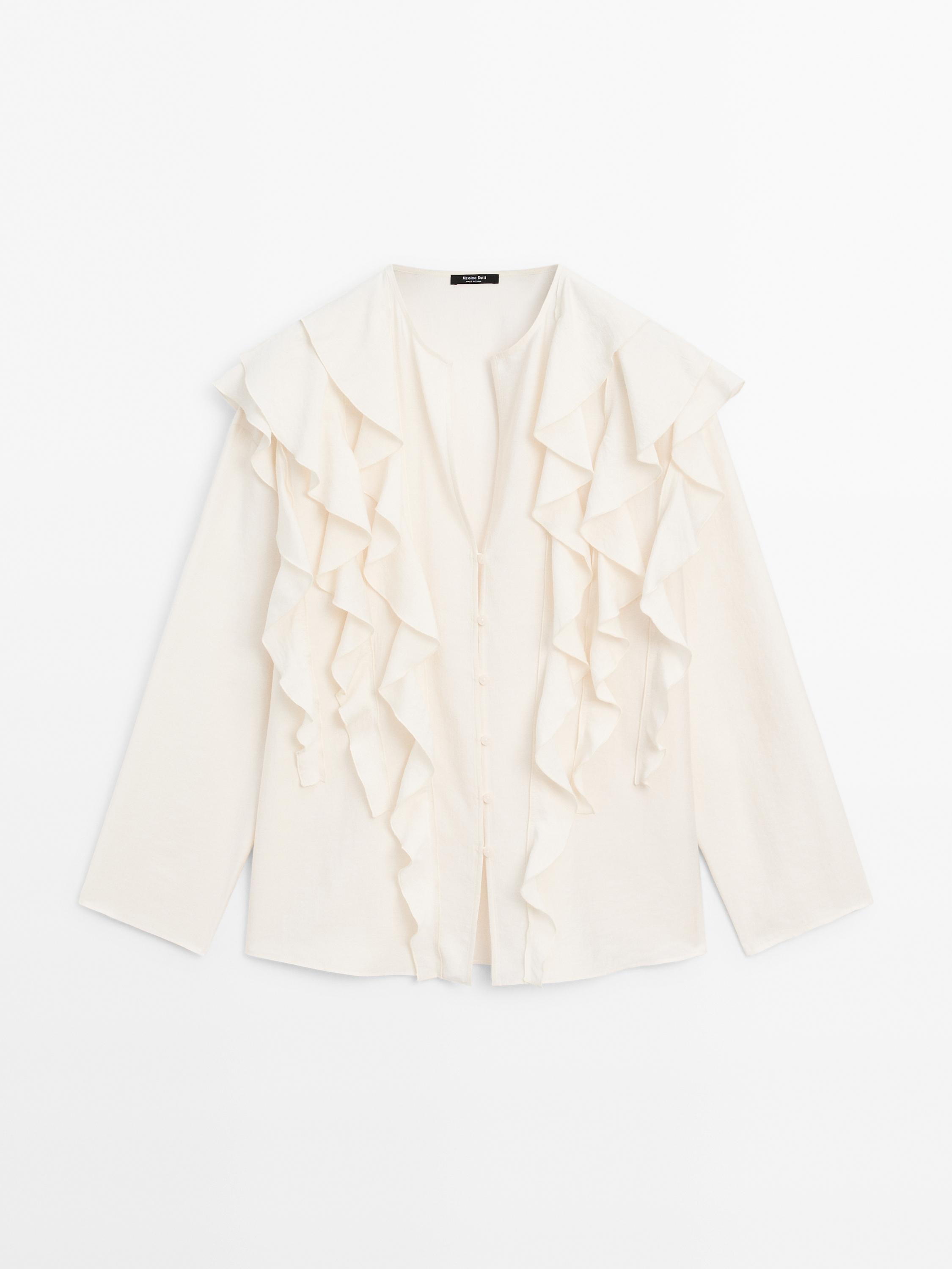 Pogled od spredaj na belo, tekočo bluzo z volančki na prsih in ramenih, skrito zapiranje na gumbe in dolge rokave.