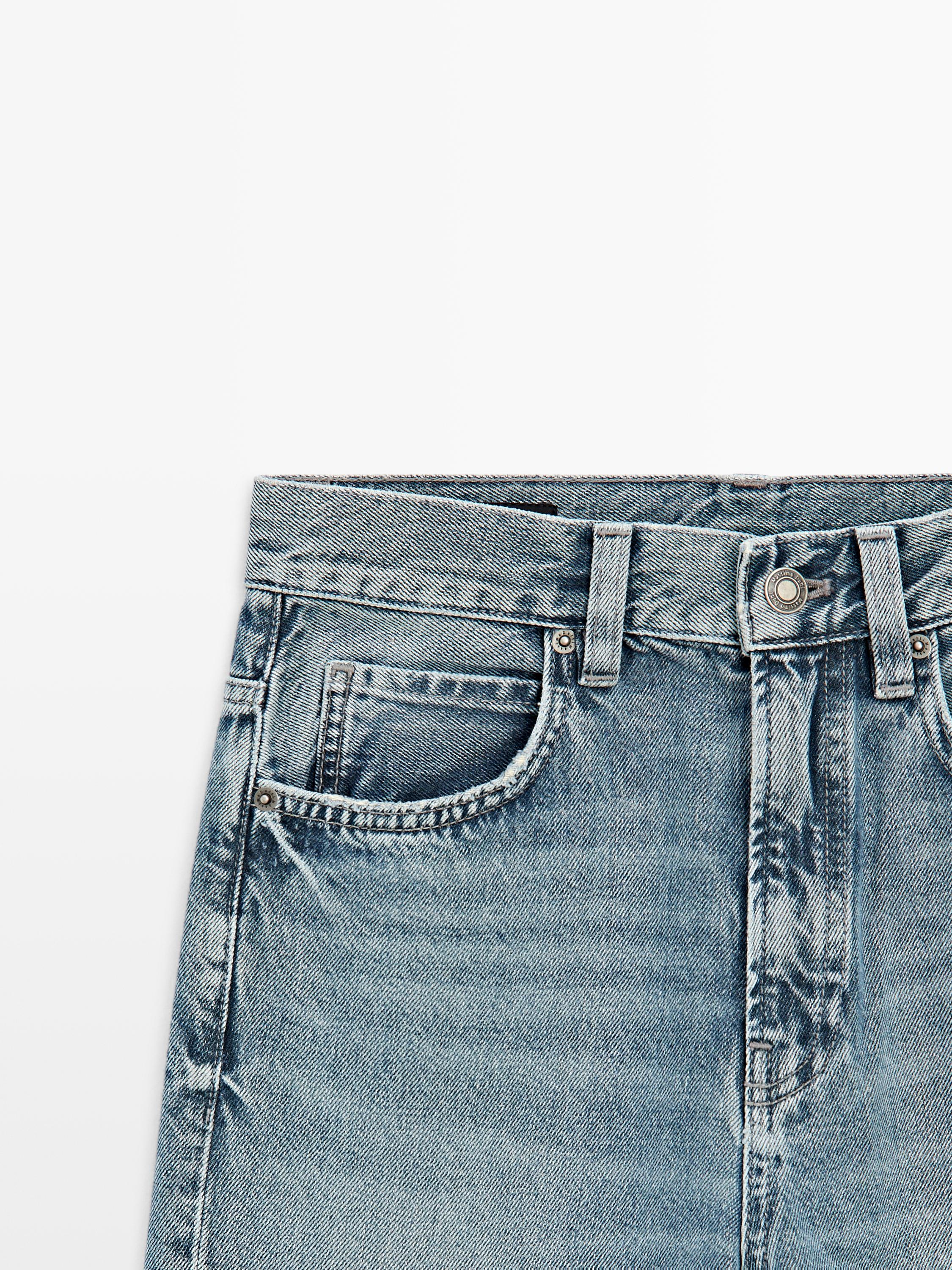 Halflange close-up van lichtblauwe high-waist jeans met riemlussen en zichtbare zijzak.