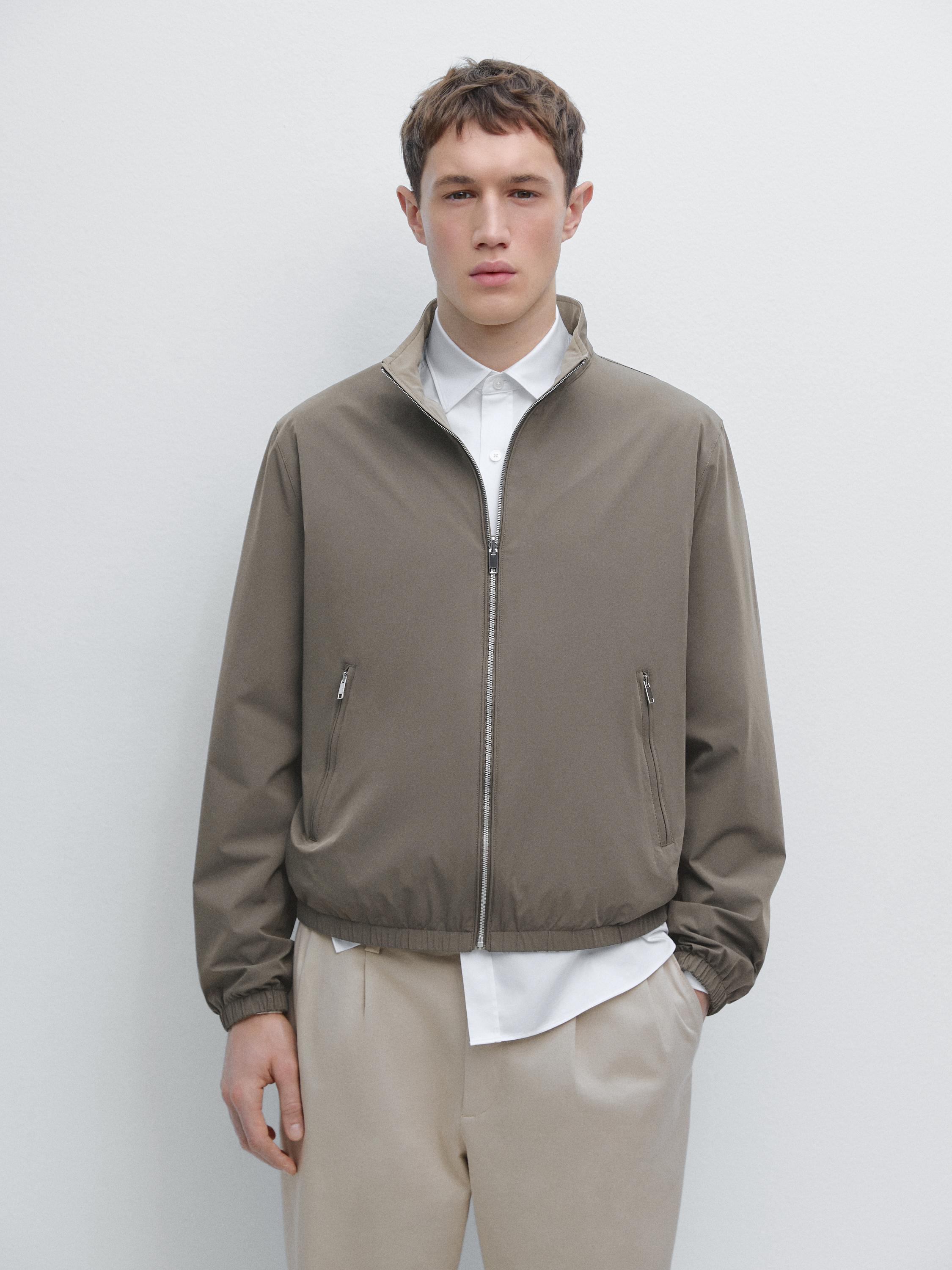 Ensemble composé d'une veste grise zippée avec poches latérales, d'une chemise blanche et d'un pantalon beige.