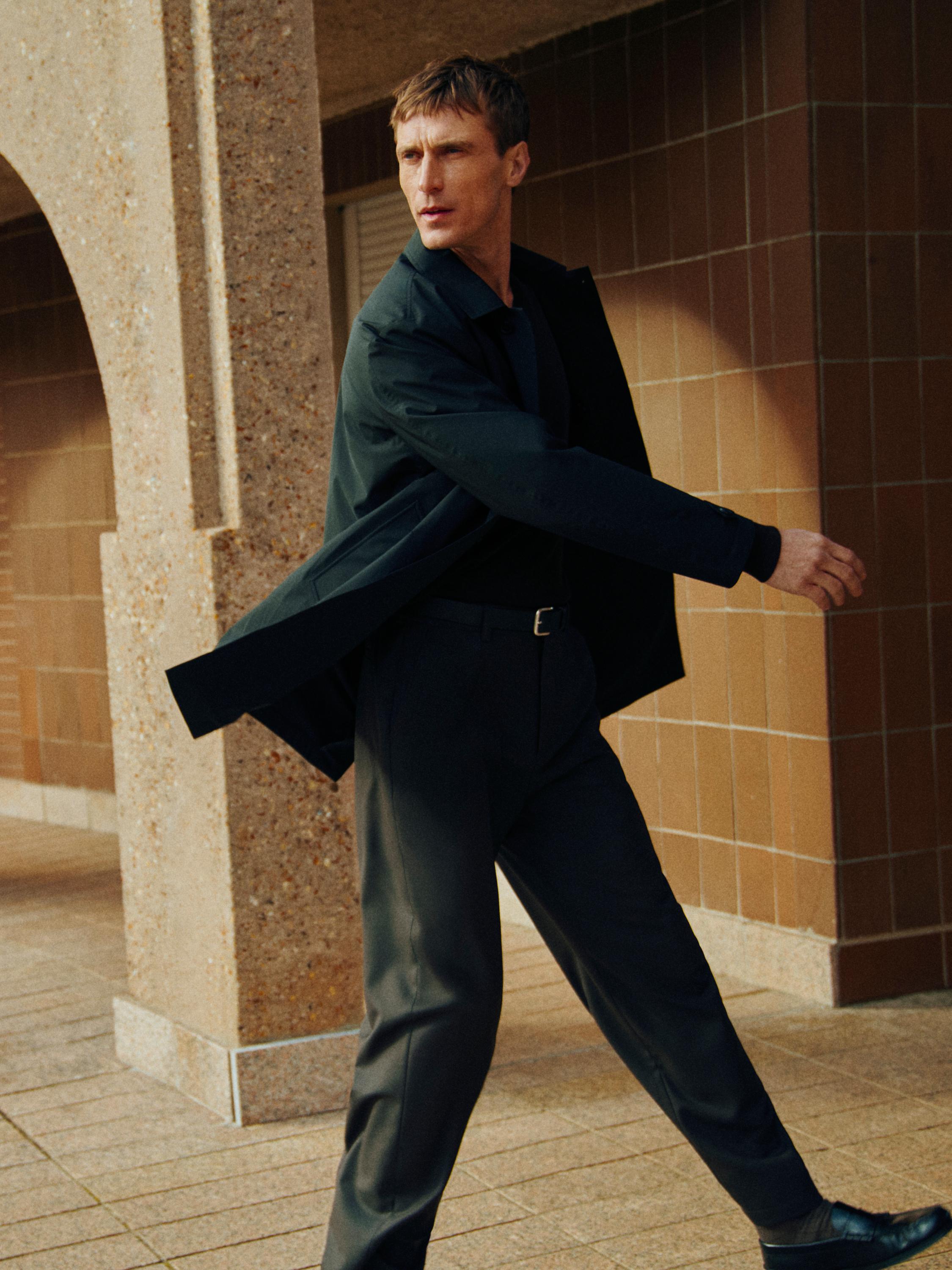 طقم مكون من معطف أسود وقميص داكن وبنطلون رمادي.