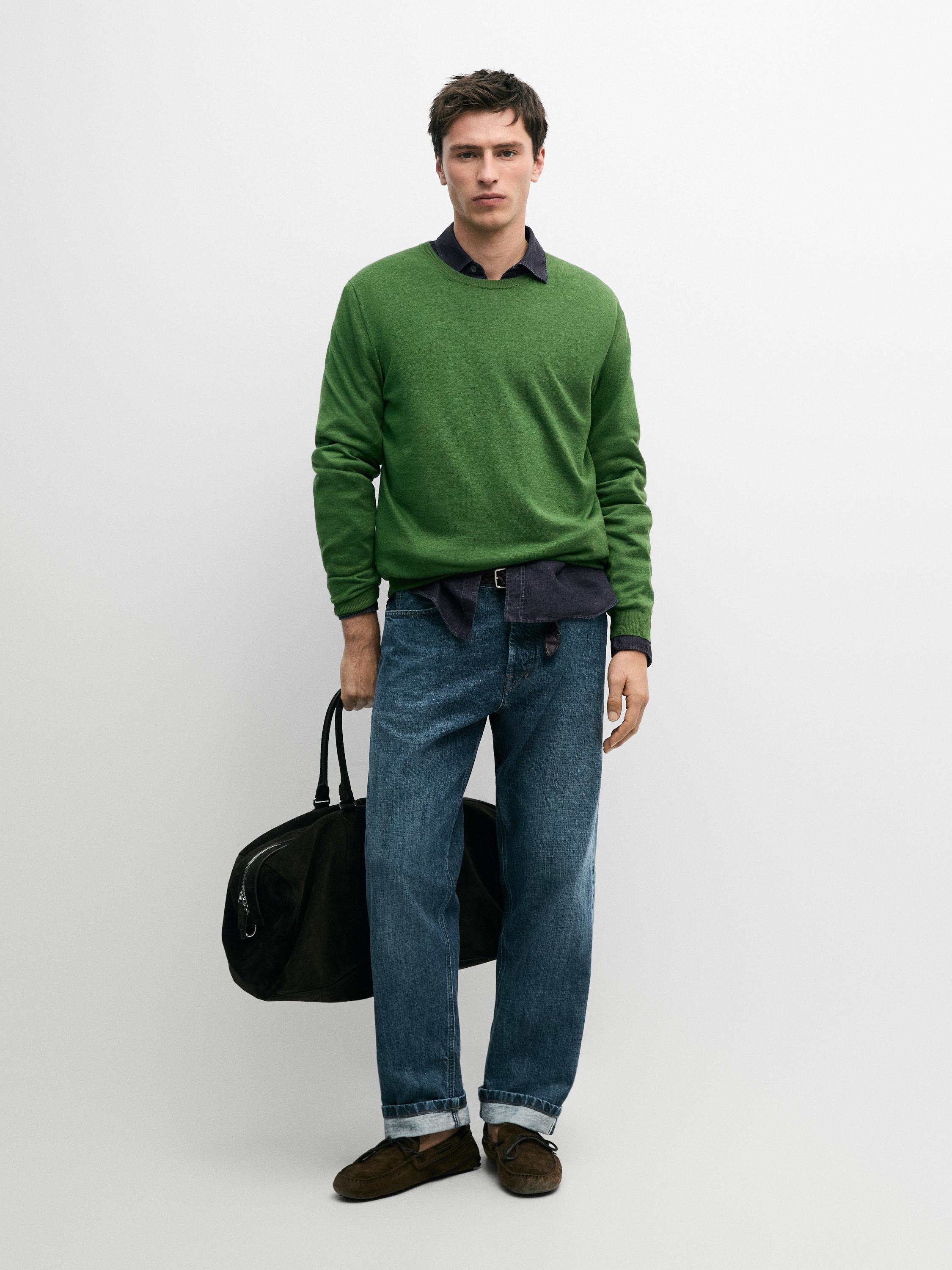 Grüner Pullover, dunkles Hemd und gerade Indigo-Jeans.