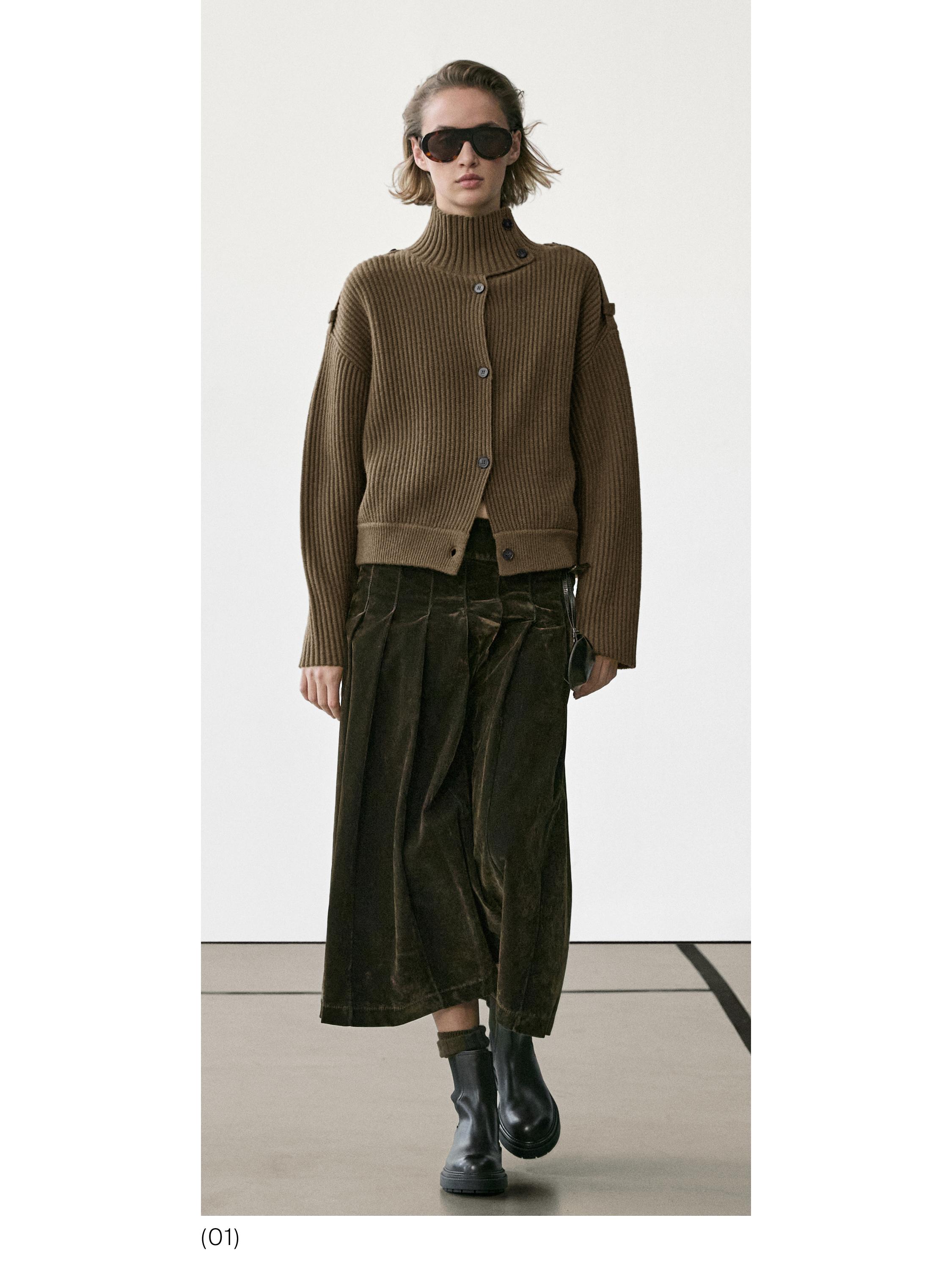 Conjunto de chaqueta café de punto con botones, falda larga plisada verde oscuro y botas negras.