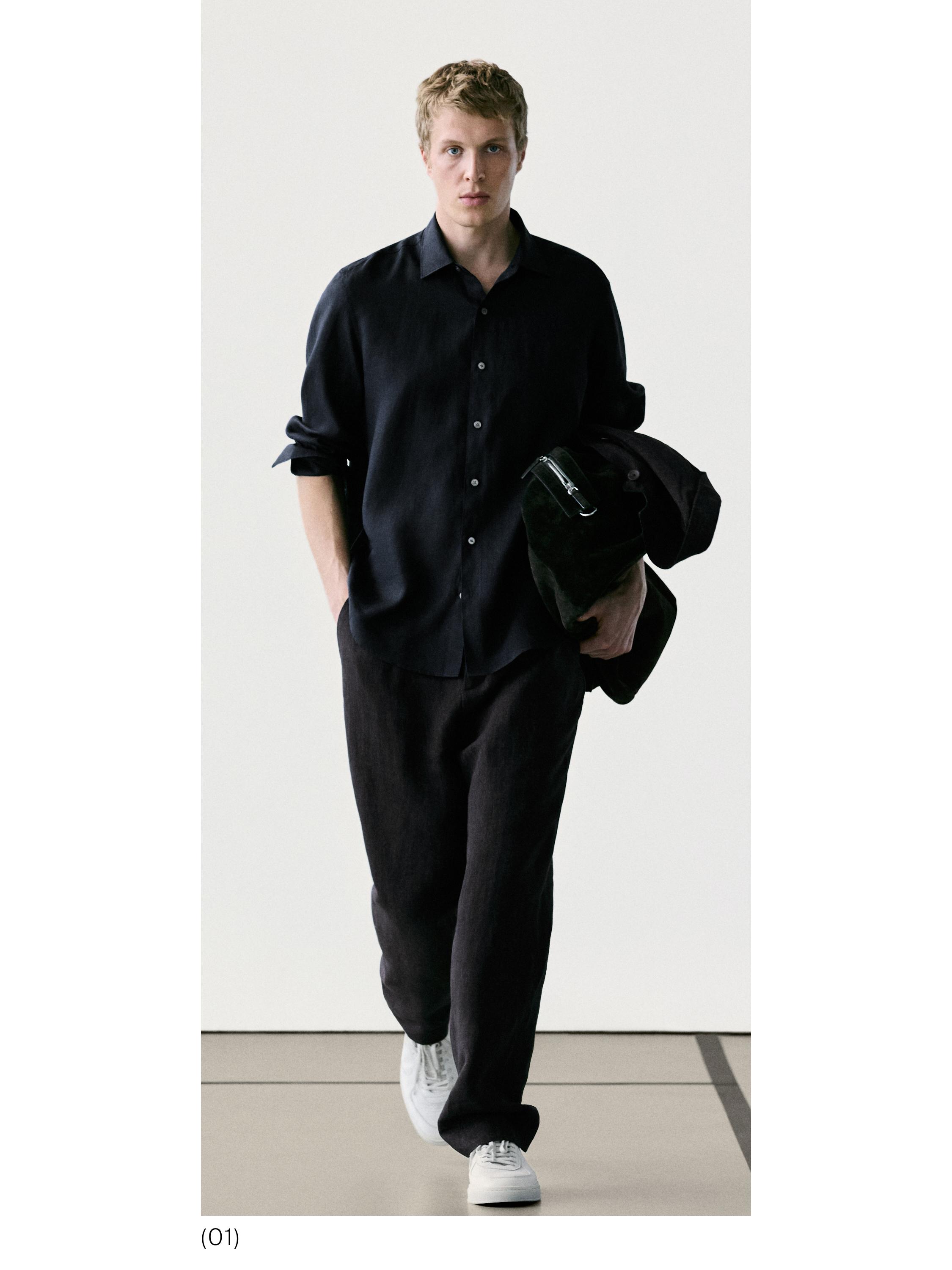 Zwarte overhemdset met knopen en losse zwarte broek. Witte sneakers zichtbaar.
