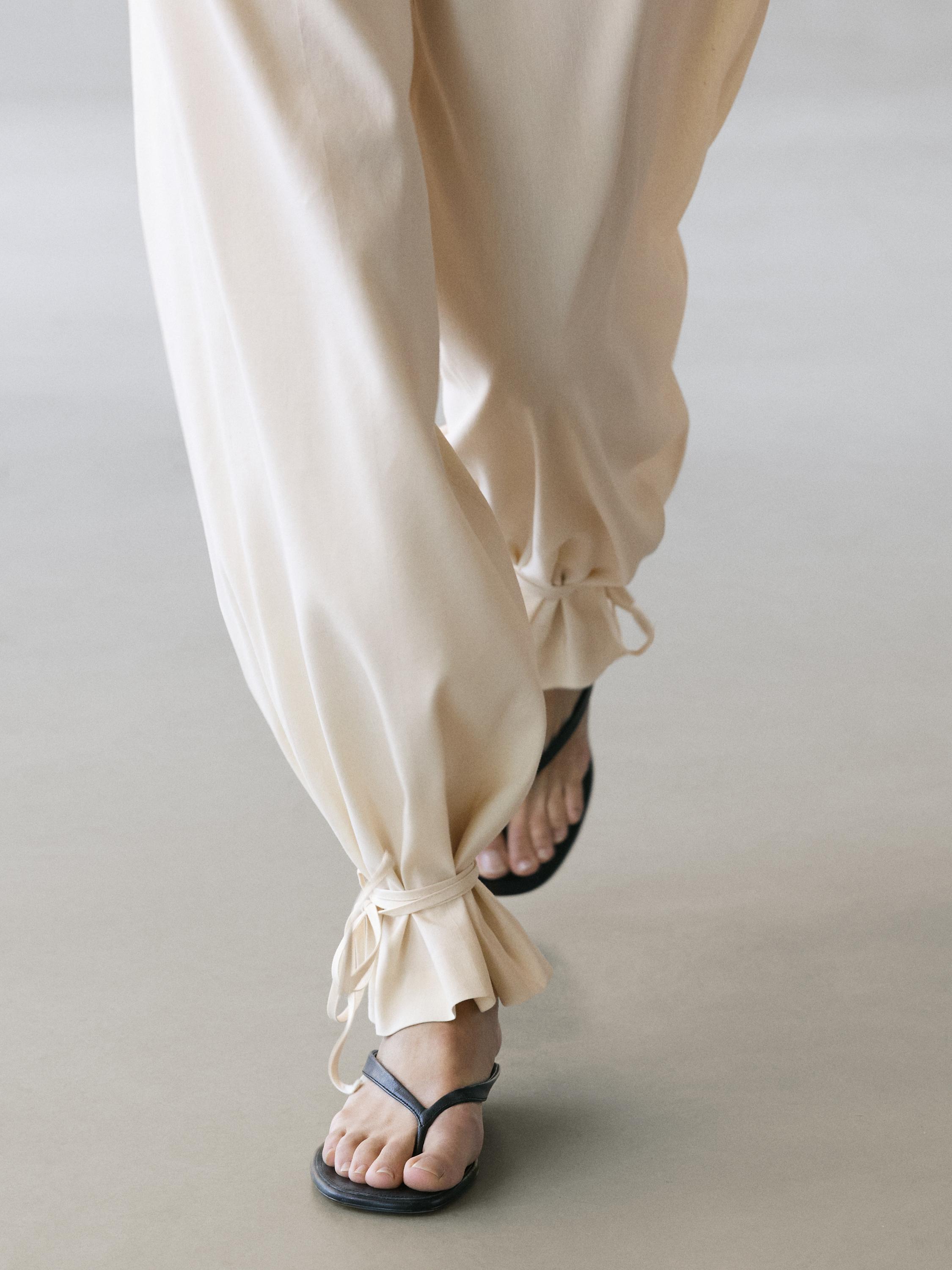 Primeiro plano de pantalóns crus con lazos nos nocellos.