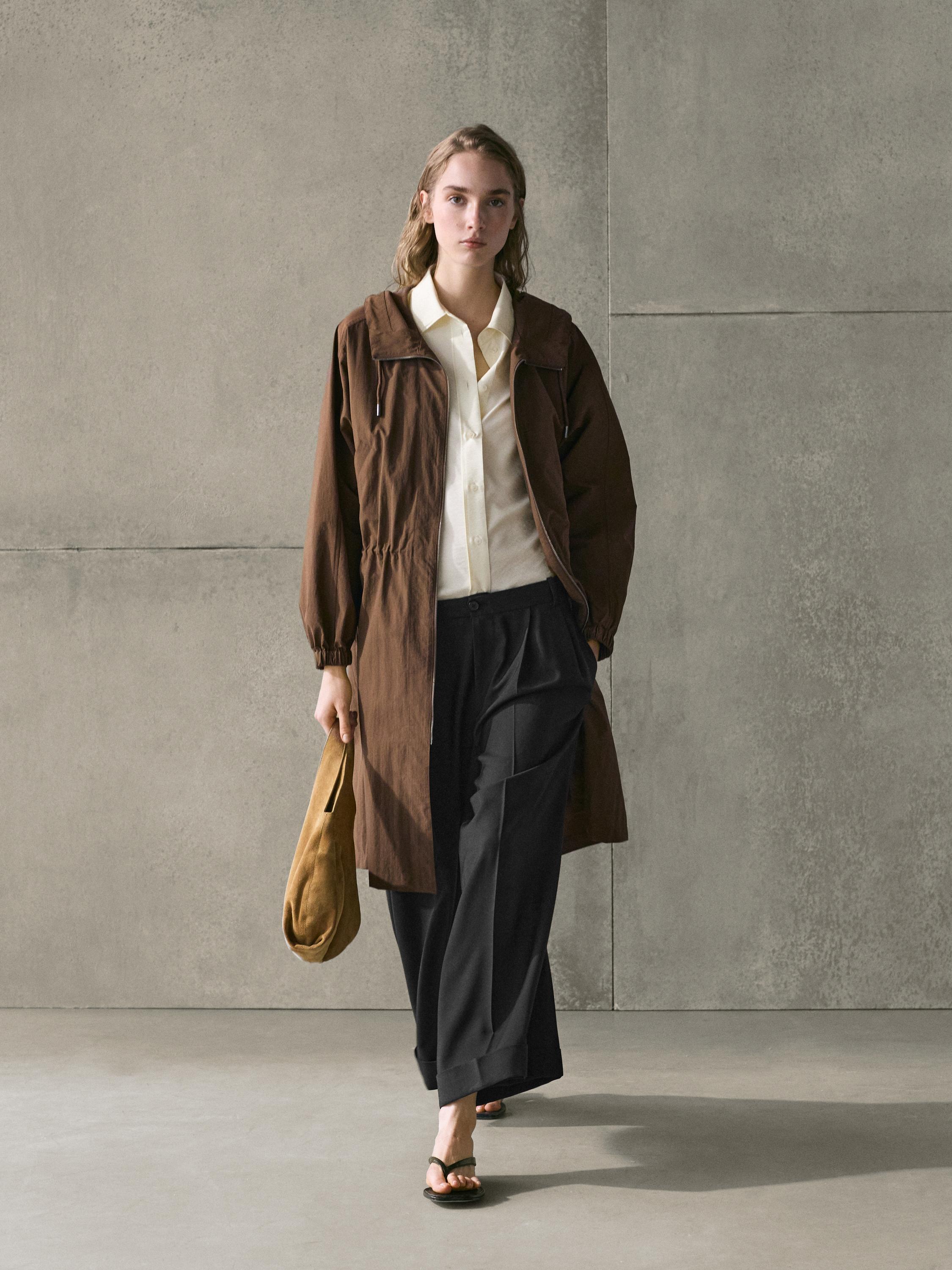 Long brown parka set with pockets, white shirt, and wide black pants.