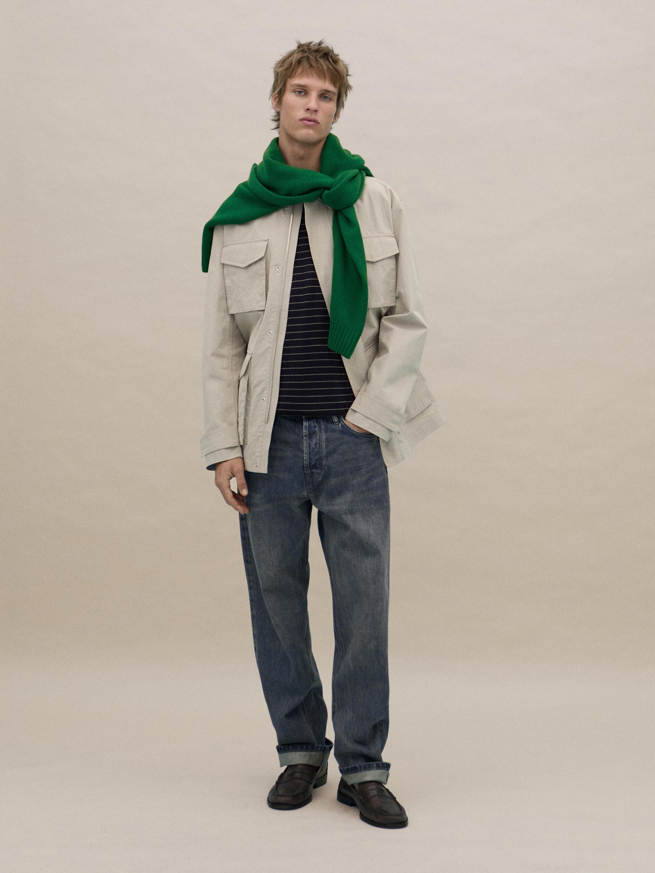 Ensemble composé d'une veste beige à poches avant, d'une écharpe verte, d'un t-shirt à rayures noires et d'un jean bleu.