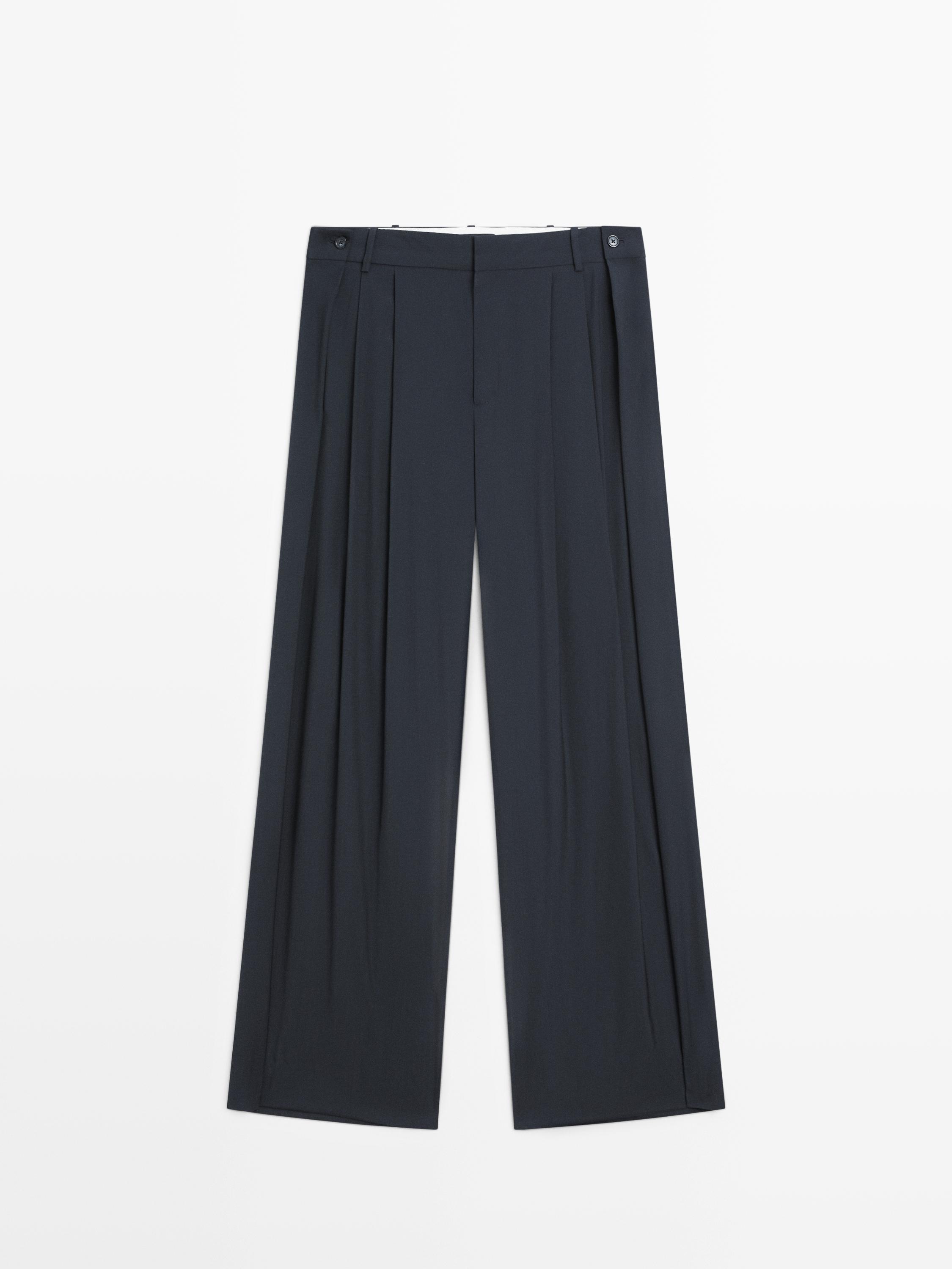 Front view of navy blue pants with pleats and button closure at the waist.