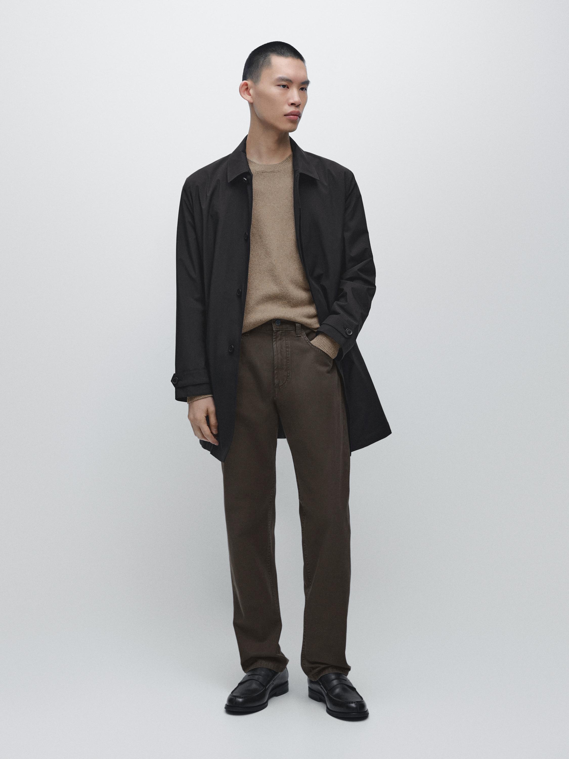 Conjunto de casaco preto, camisola bege e jeans castanhos descontraídos.